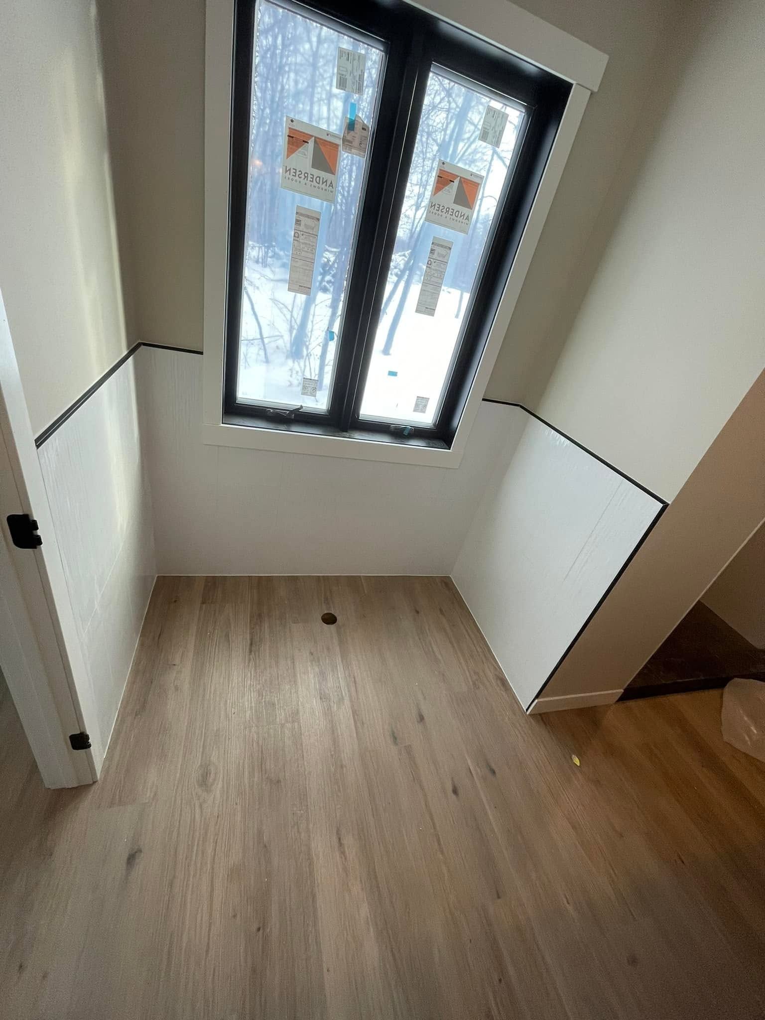 Empty small room with wood floor, white walls, and a window at the far end.