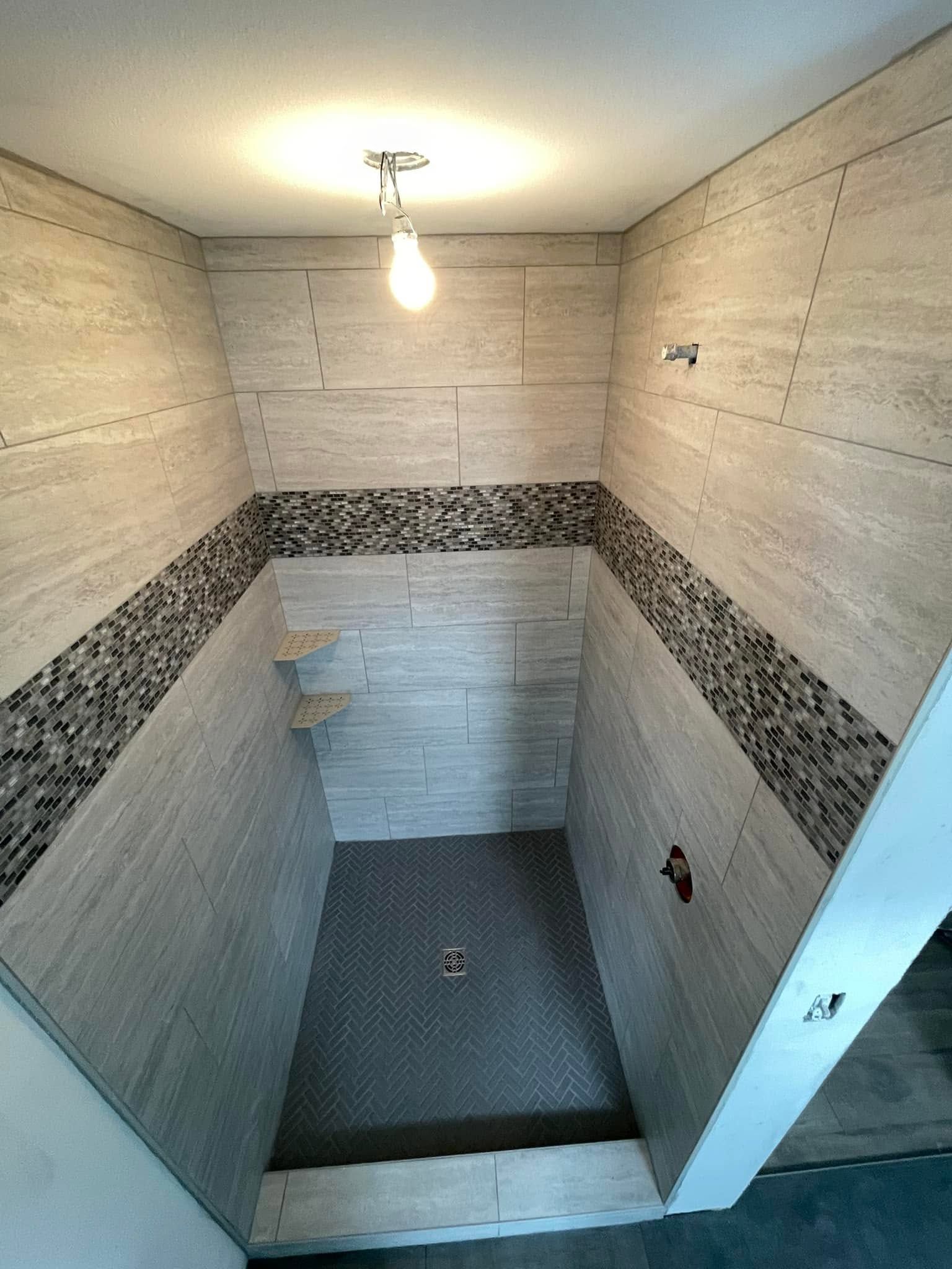 Empty tiled shower stall with a mosaic accent band and a single light bulb overhead.