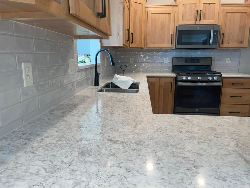 Bright kitchen with granite countertop, wooden cabinets, stainless stove, microwave, and sink beneath a window