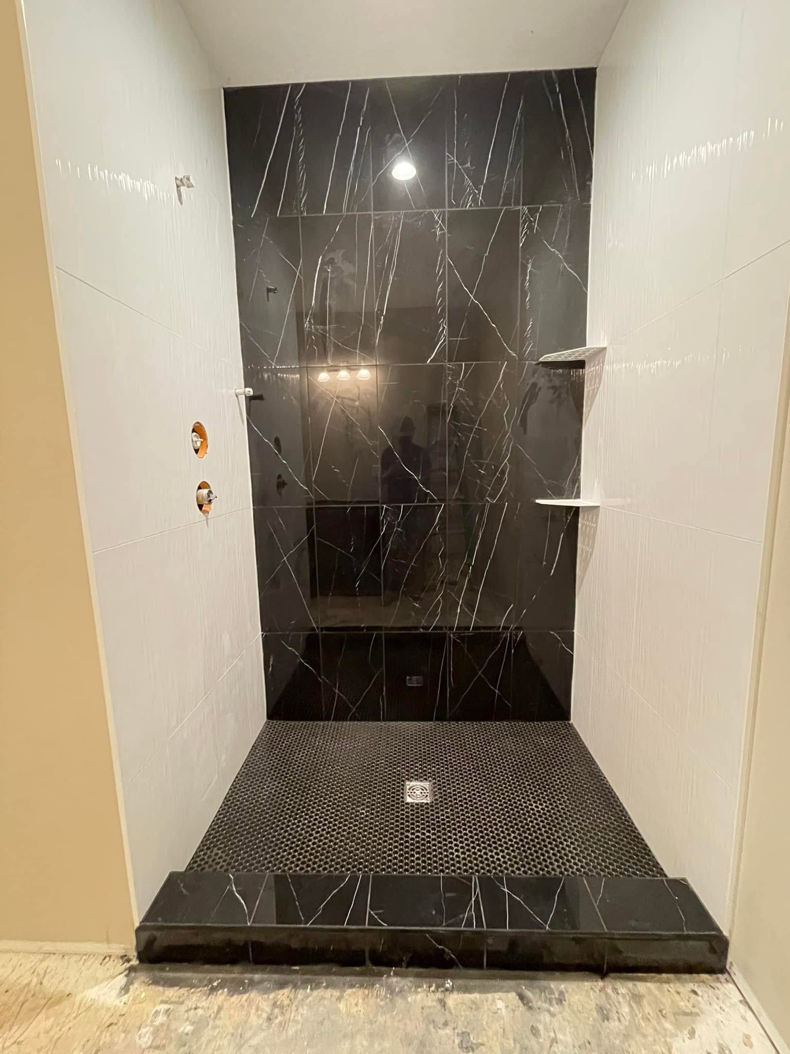 Modern black-and-white shower stall with tiled floor, marble-look wall, and glass partition shelves
