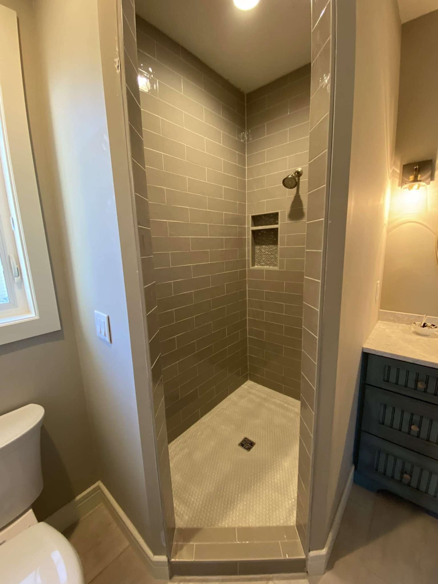 Modern walk-in shower with gray tile, white floor, and built-in niche in a bathroom