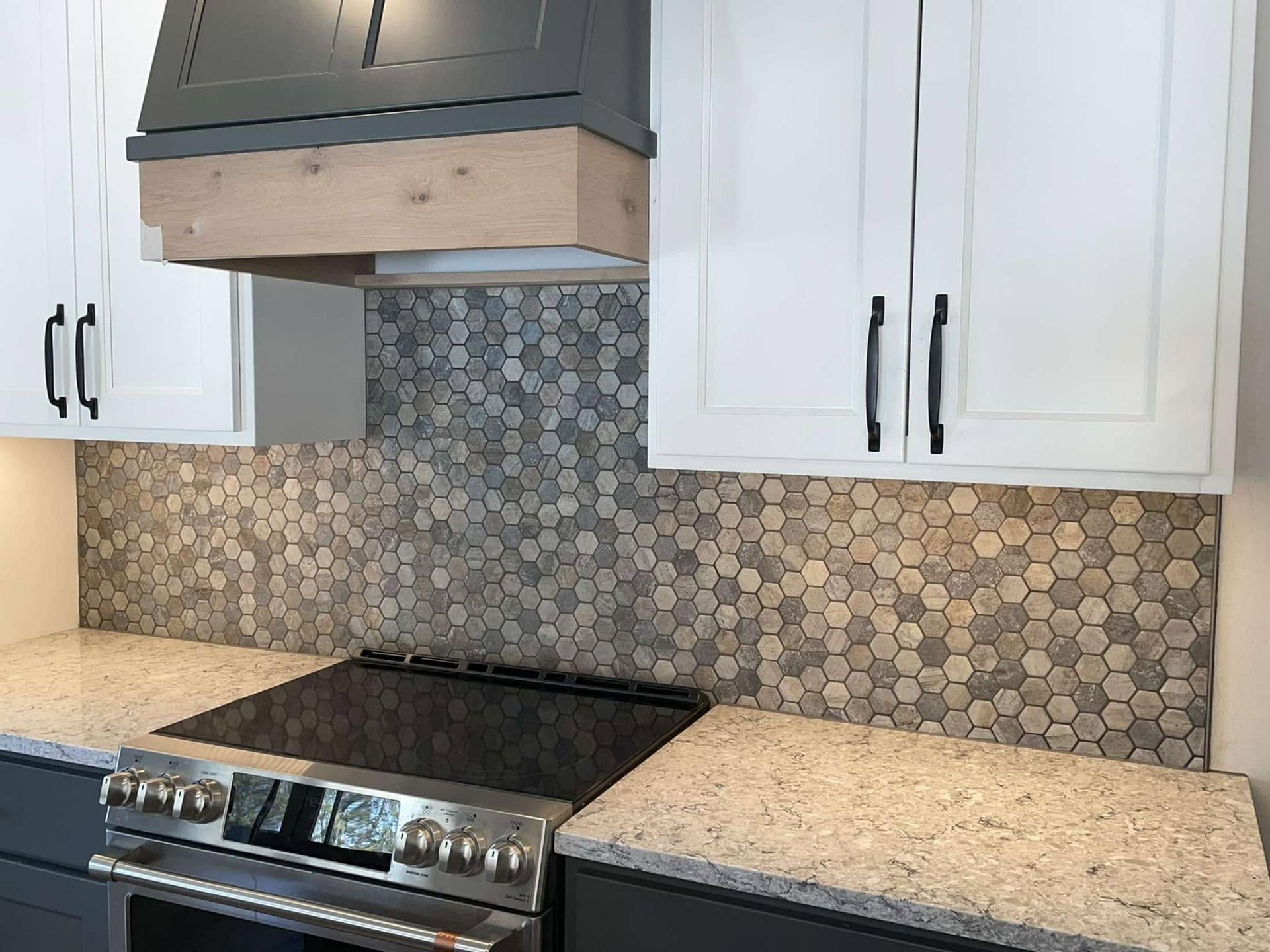 Modern kitchen with white cabinets, black range hood, mosaic tile backsplash, and stainless steel stove.