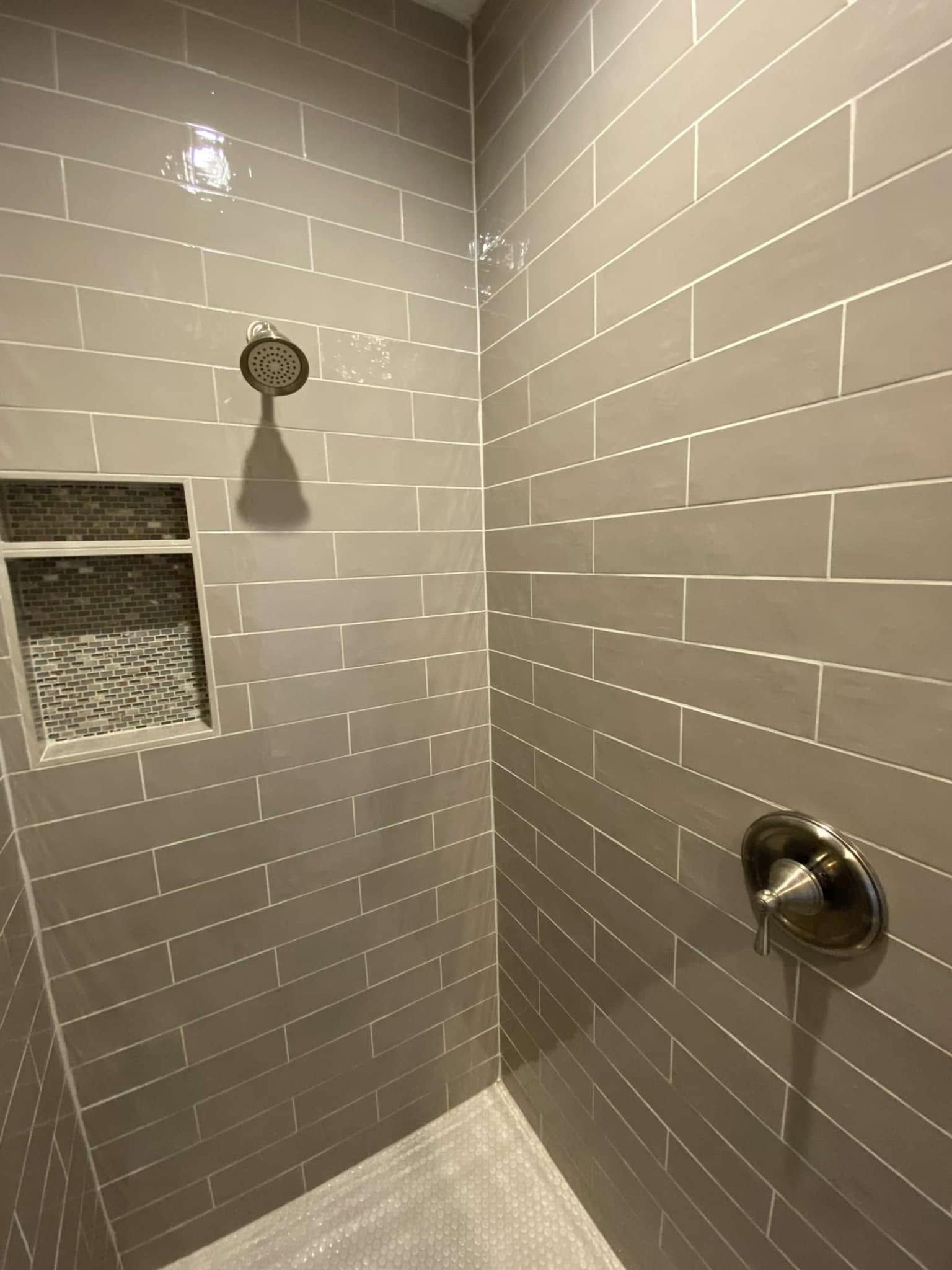 Empty tiled shower with chrome fixtures and a built-in soap niche.
