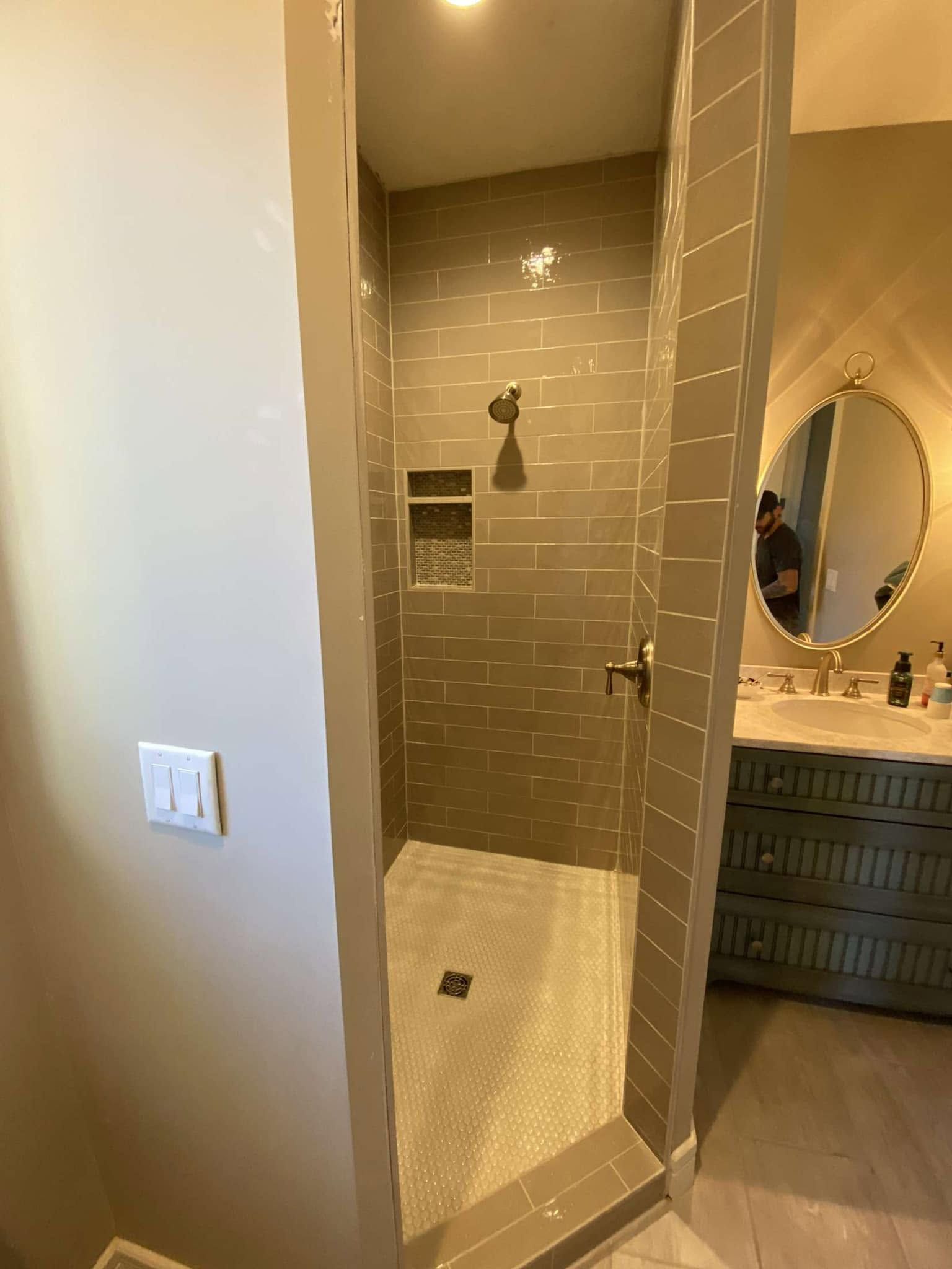 Small tiled walk-in shower beside a vanity and mirror in a bathroom
