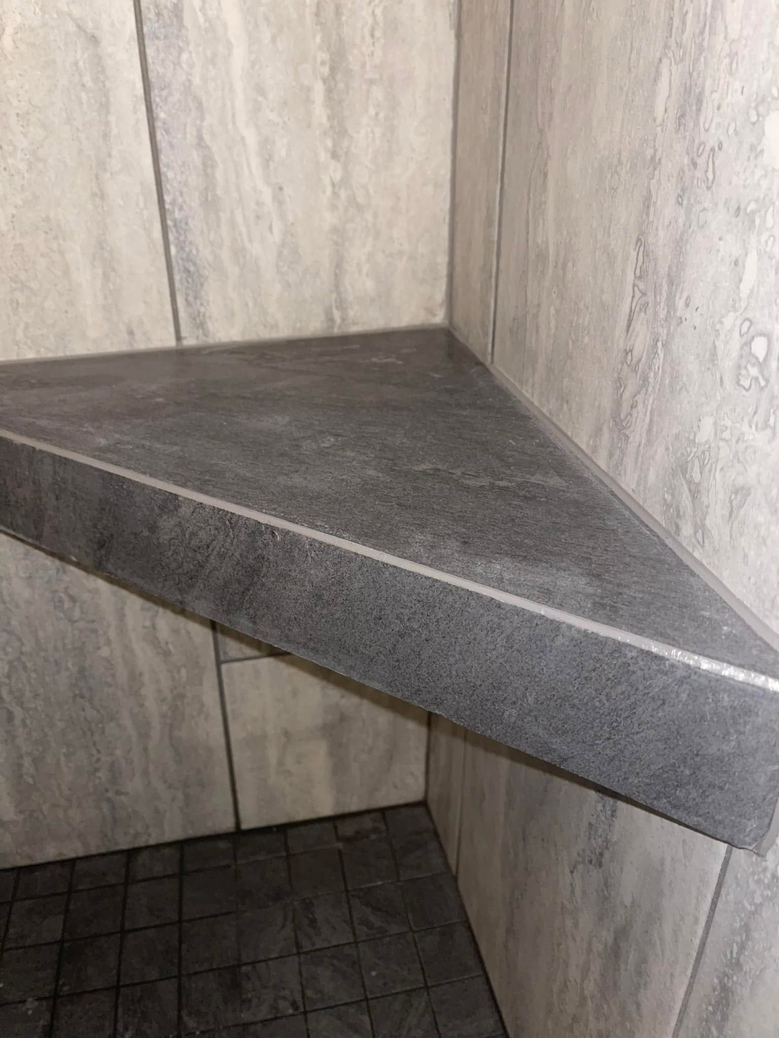 Corner shower bench with dark stone seat and tiled walls inside a bathroom