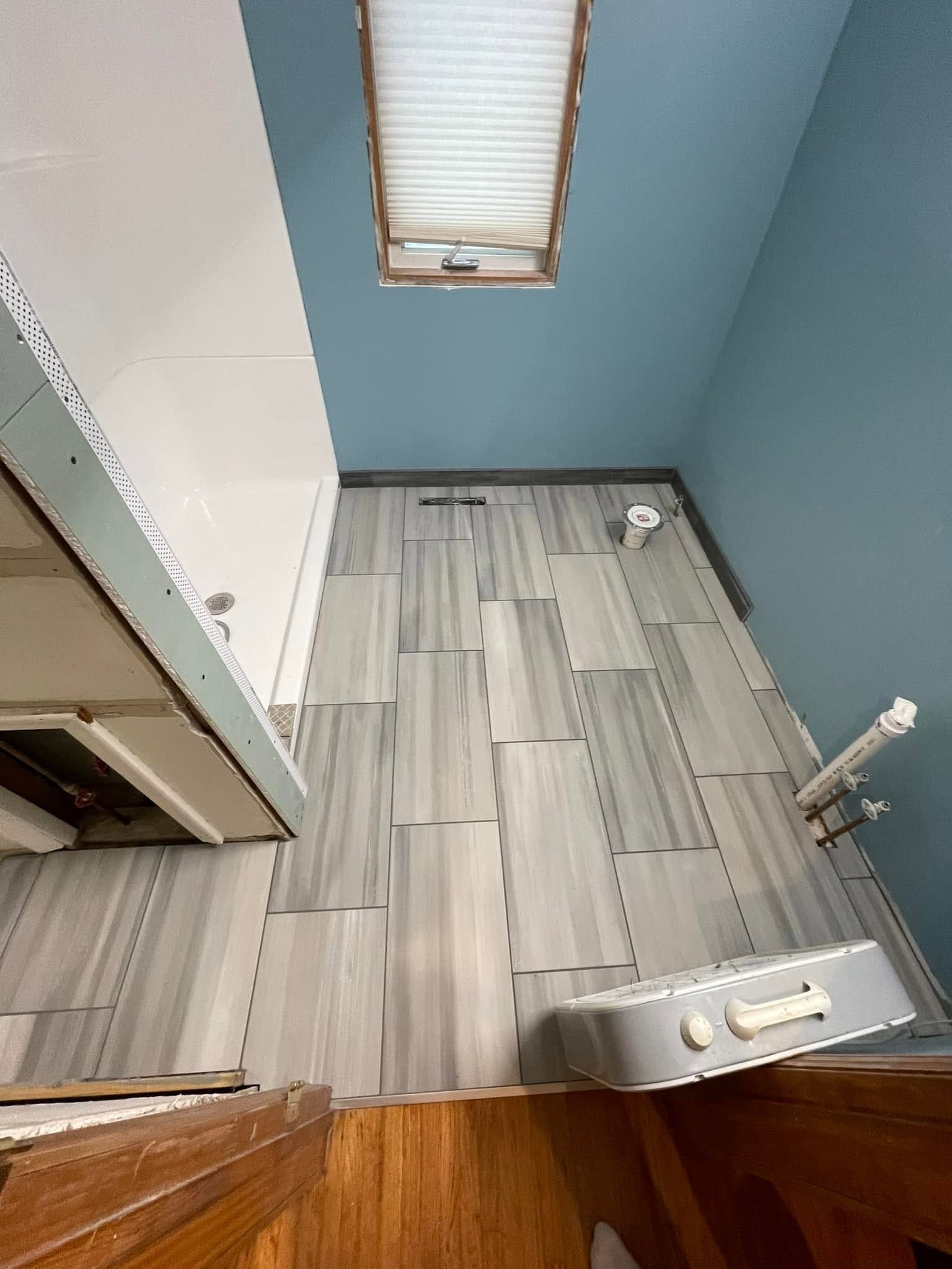 Small bathroom with blue walls, gray wood-look tile floor, toilet, and wooden door at the bottom.