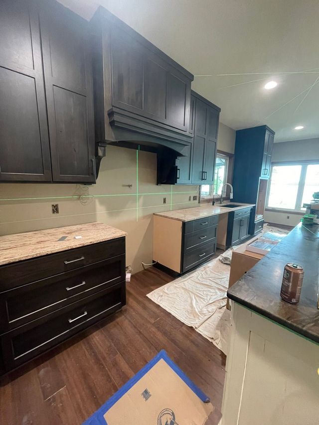 Modern kitchen with dark cabinets, granite counters, and wood floors, viewed from the entryway