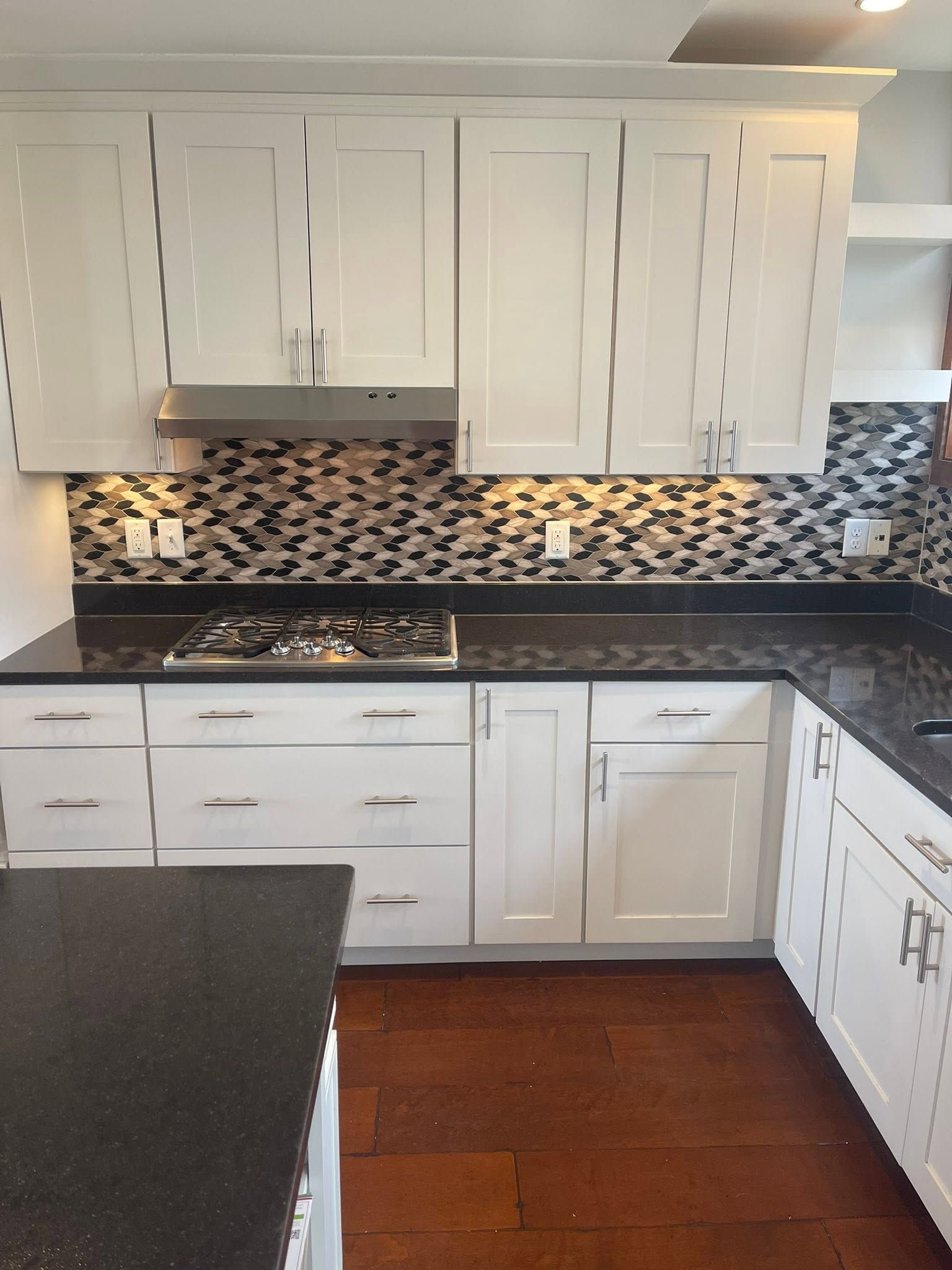 White kitchen with black countertops, mosaic backsplash, and wood floor