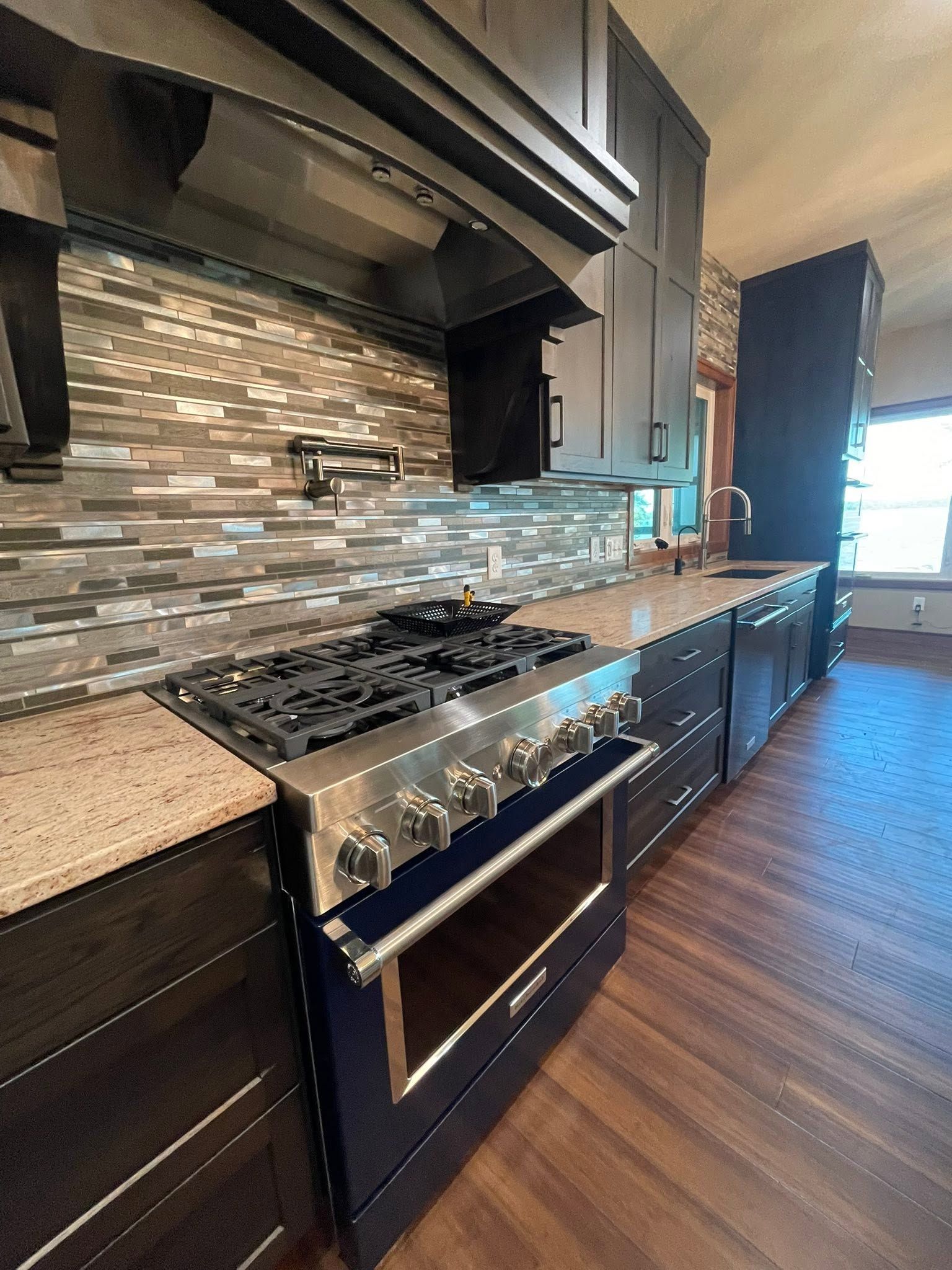 Modern kitchen with stainless steel range, mosaic tile backsplash, dark cabinets, and wood flooring