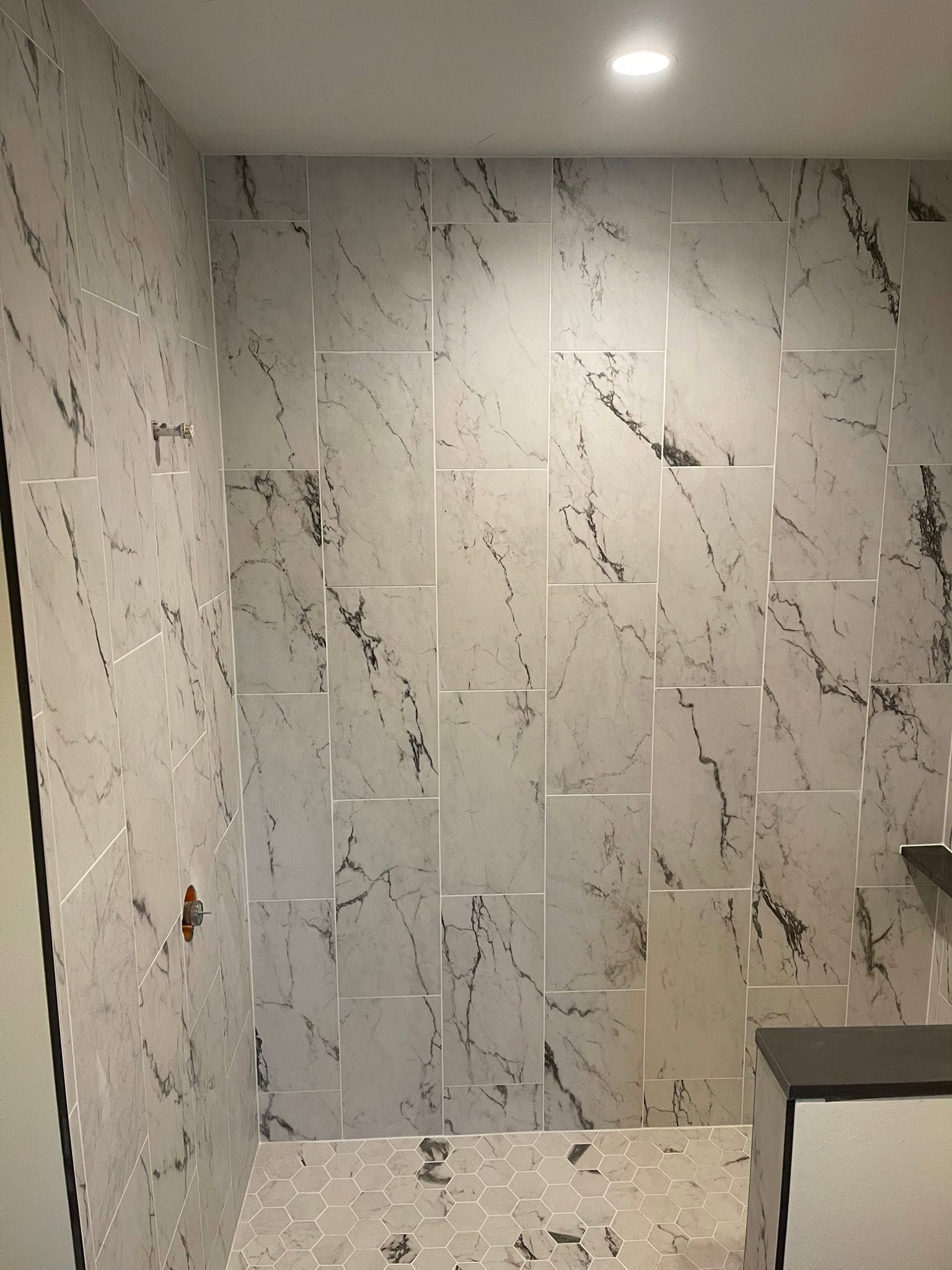 Marble-tiled bathroom with a shower and built-in shelf under a recessed ceiling light