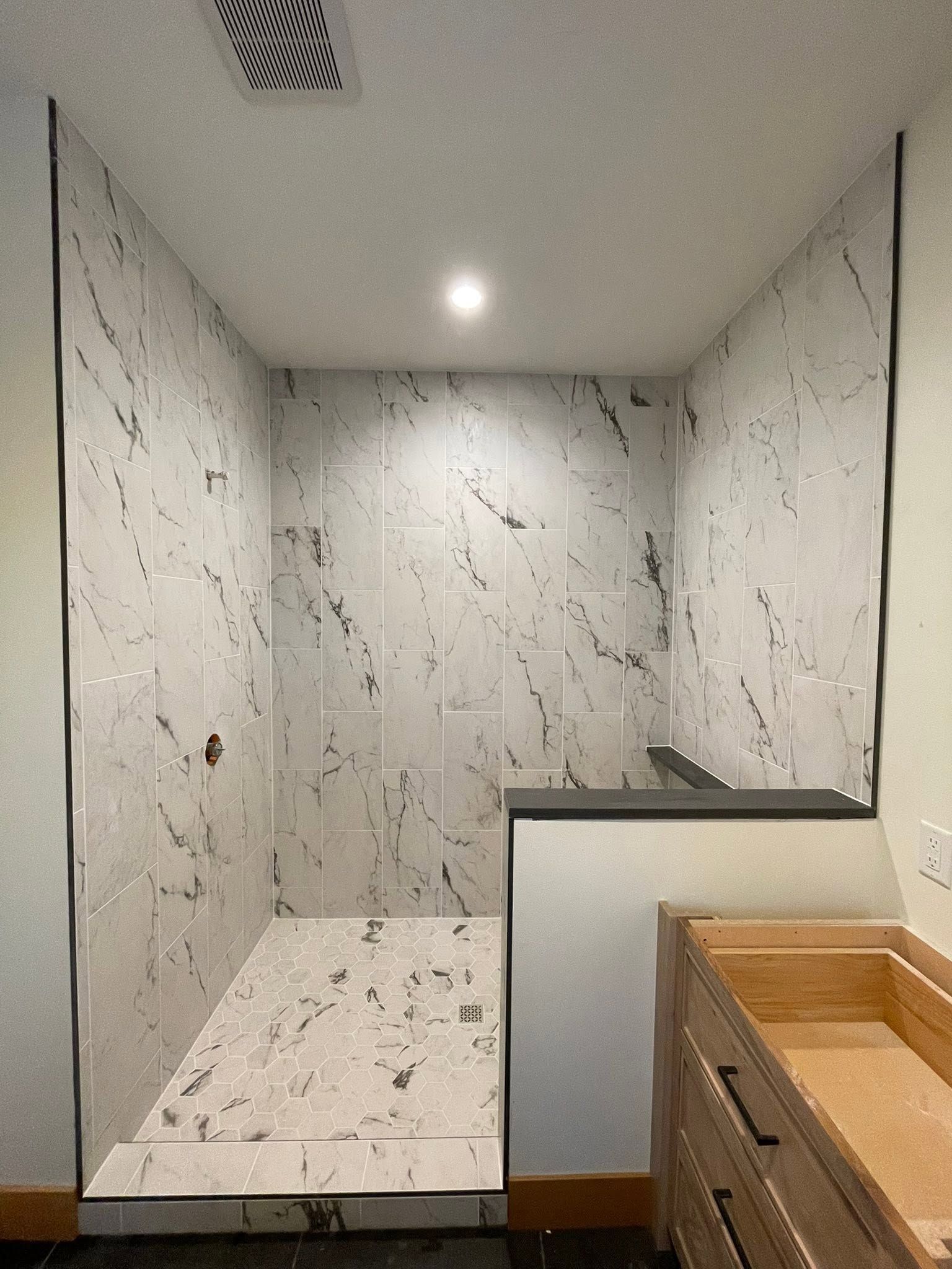 Marble-tiled shower nook with recessed shelf, ceiling light, and wood vanity edge in foreground