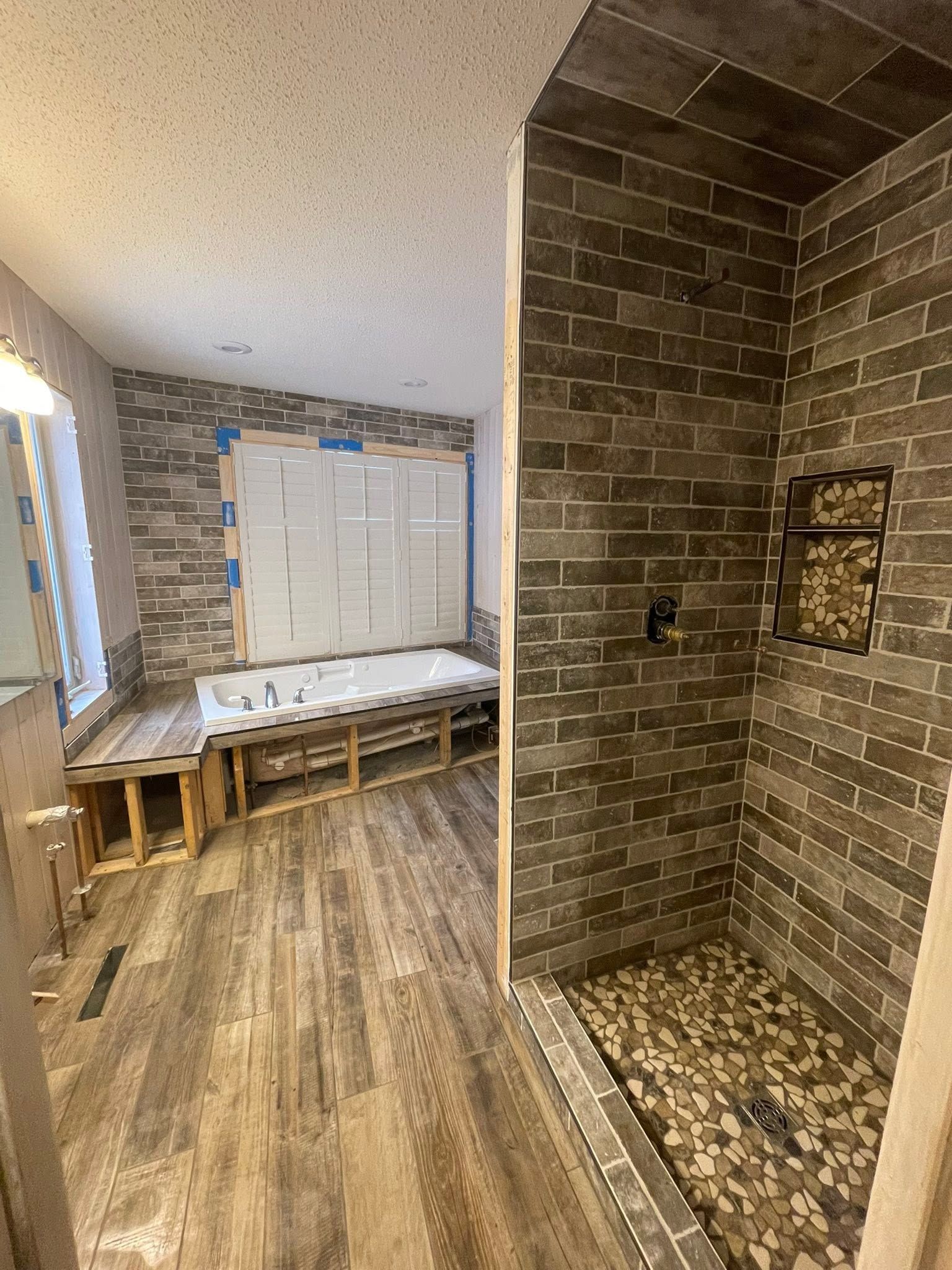 Bathroom with brick-tiled shower stall and bench beside a frosted window over wood-look flooring