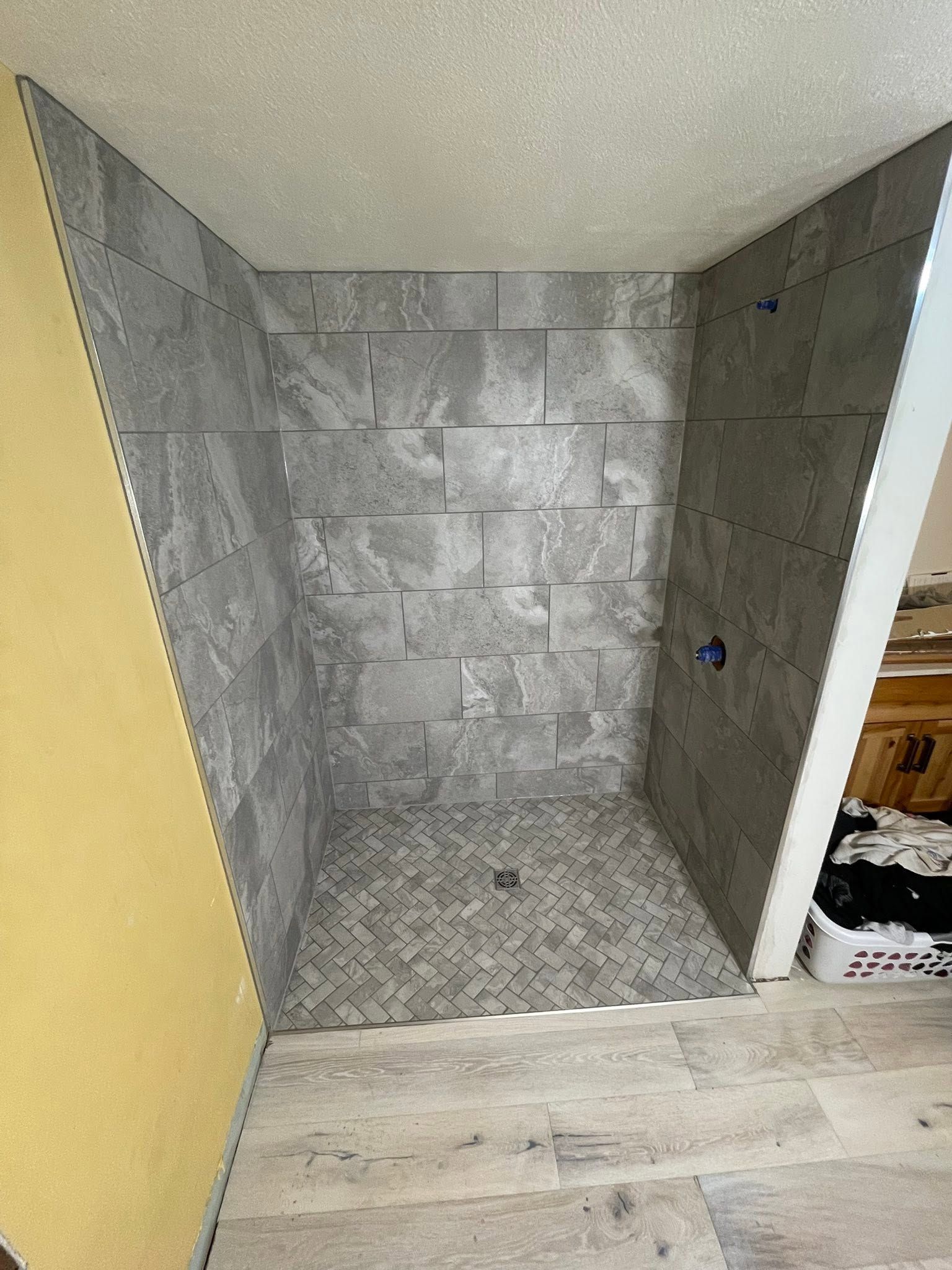 Small tiled shower stall under construction with gray stone-look walls and a yellow side wall.