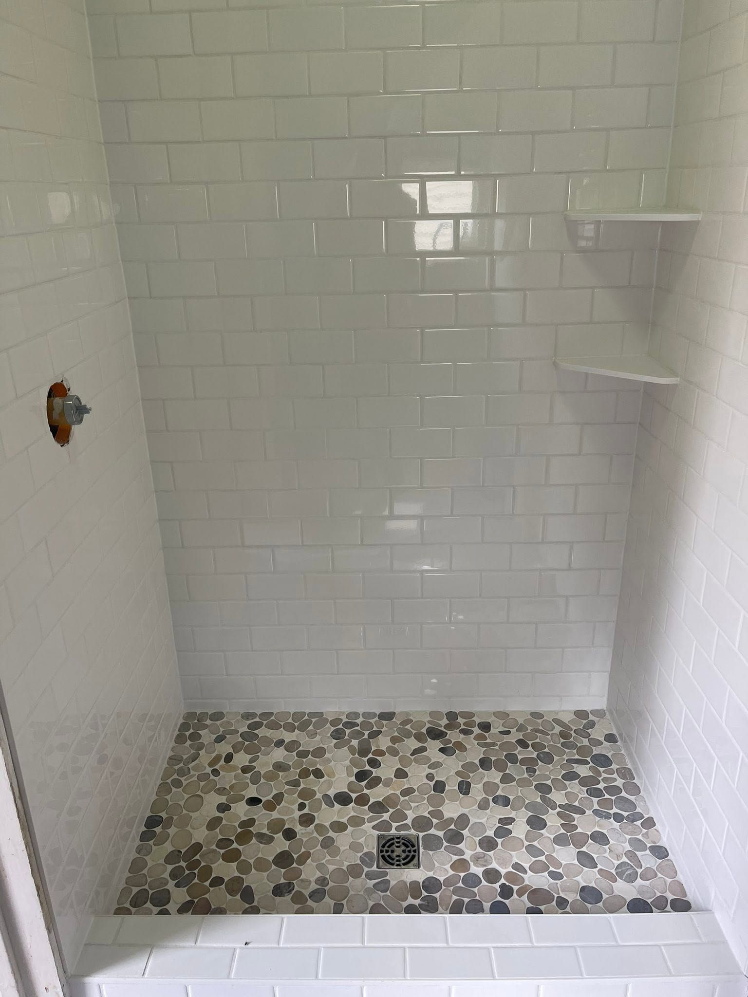 Empty tiled shower with mosaic floor, white walls, and built-in corner shelves