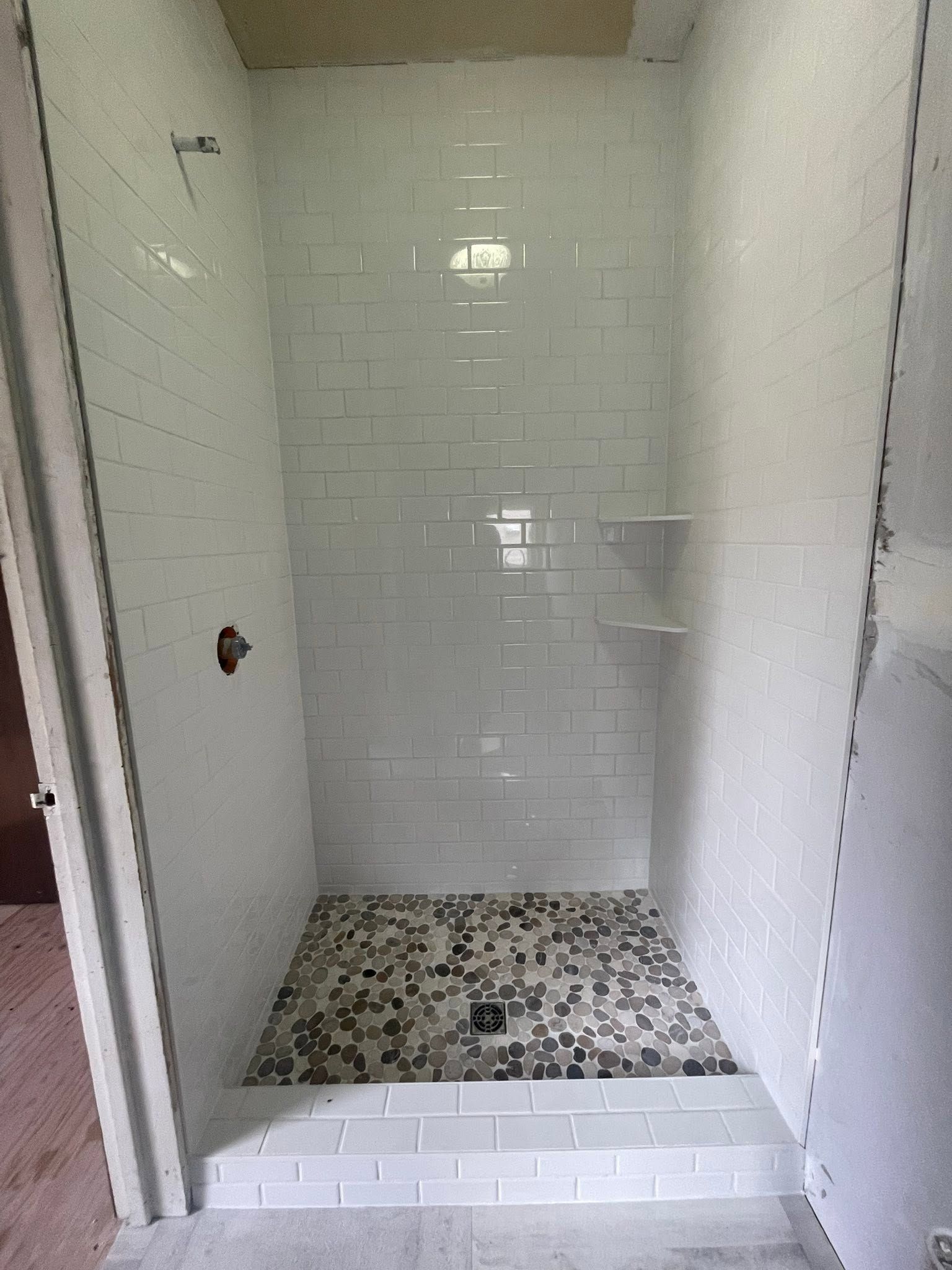 Empty tiled shower with white subway walls and a pebble floor.