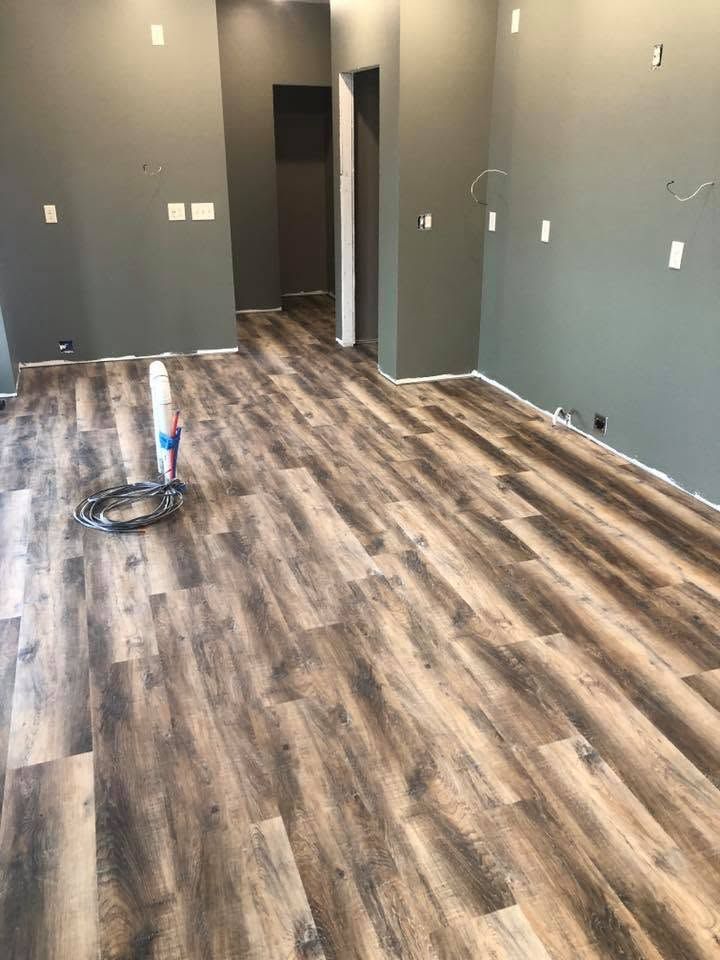 Empty room with gray walls, wood-look flooring, and a paint roller on the floor near the left wall.
