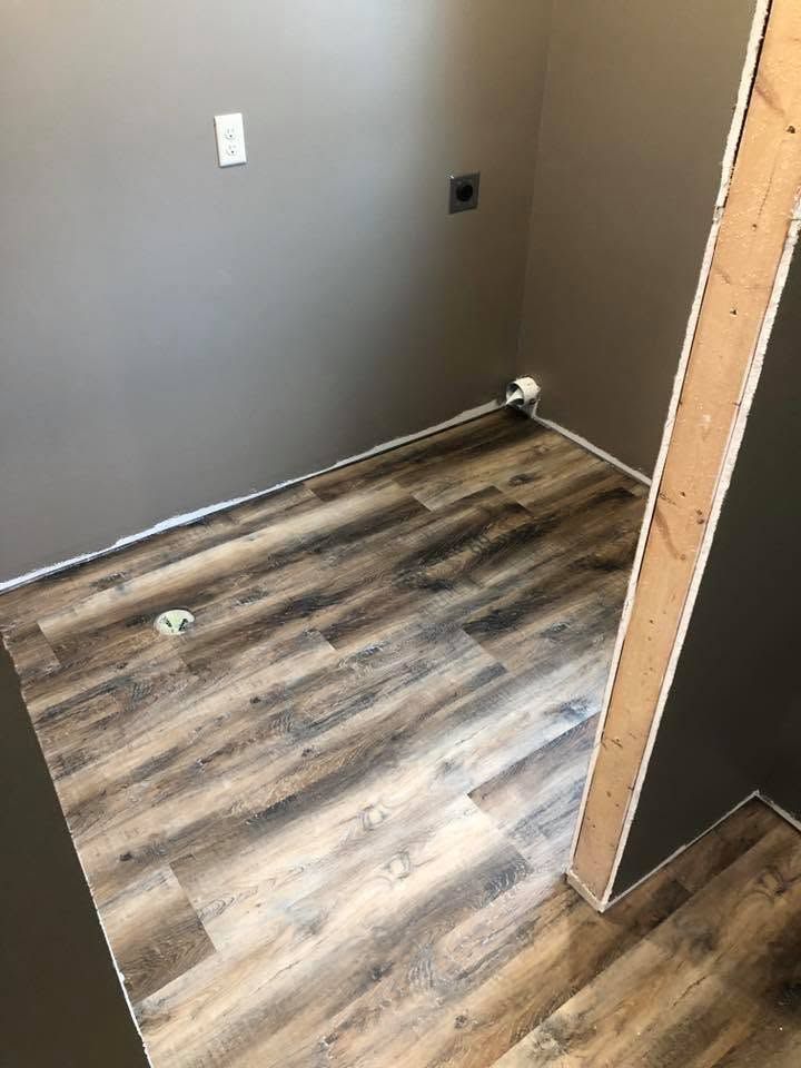 Empty small room with gray walls, wood-look flooring, and an open door frame on the right.