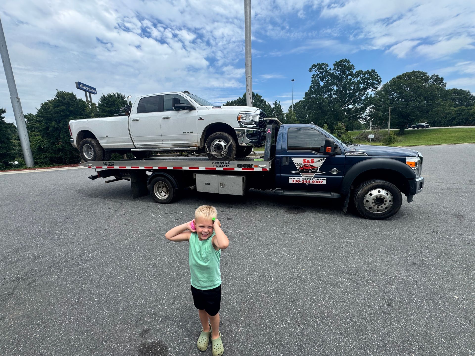 Child covers ears in front of a tow truck carrying a white pickup truck.