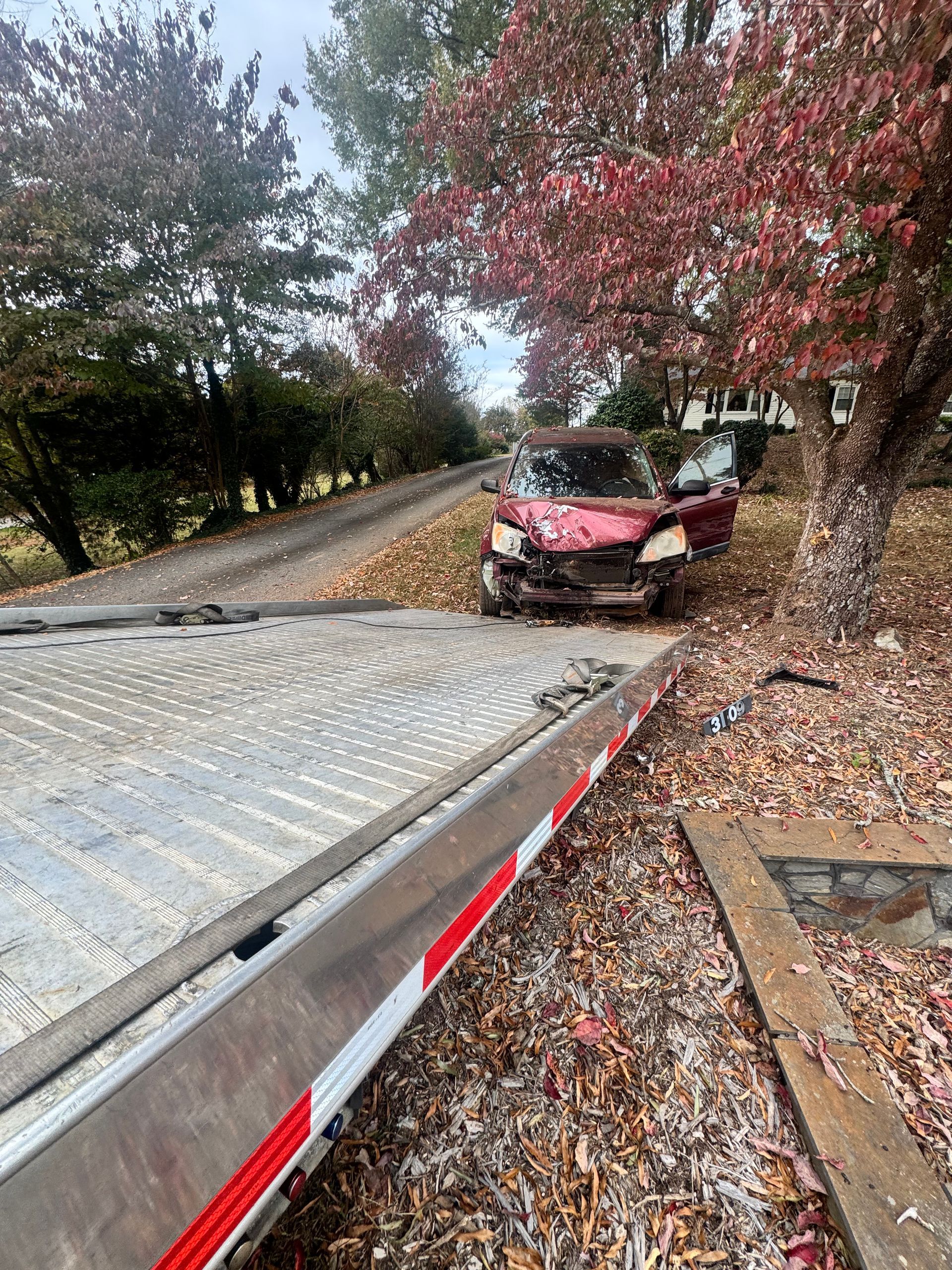 Damaged red car on a tow truck. Autumn scene with colorful leaves.