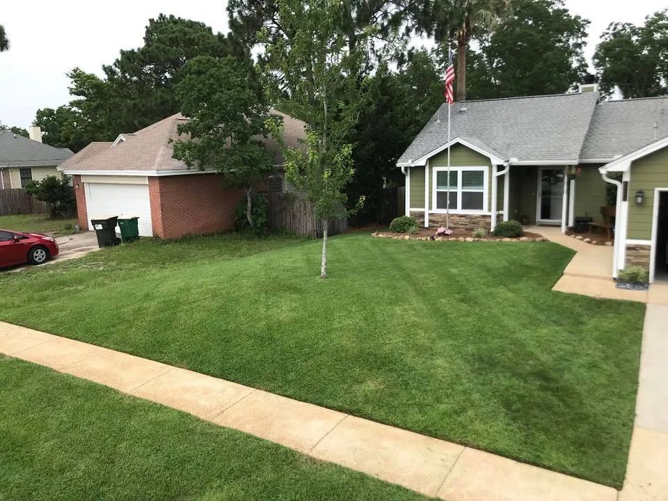 A house with a lush green lawn and a red car parked in front of it.