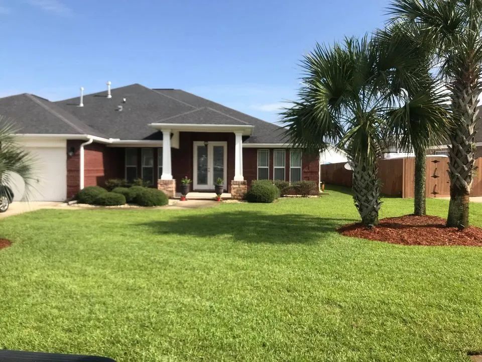 A house with a lush green lawn and palm trees in front of it.