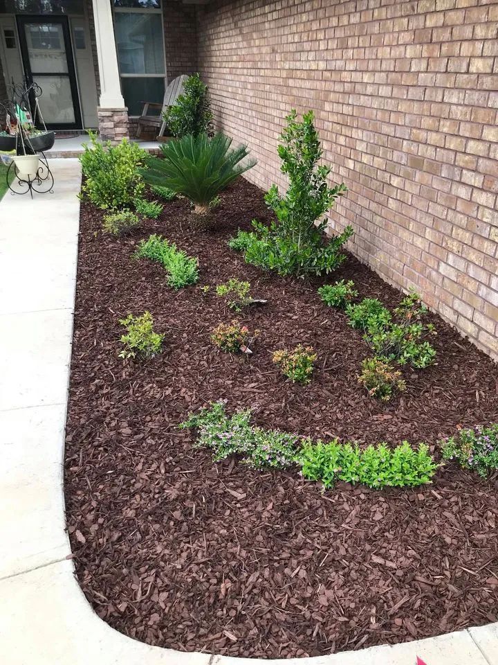 A garden with mulch and plants in front of a brick wall.