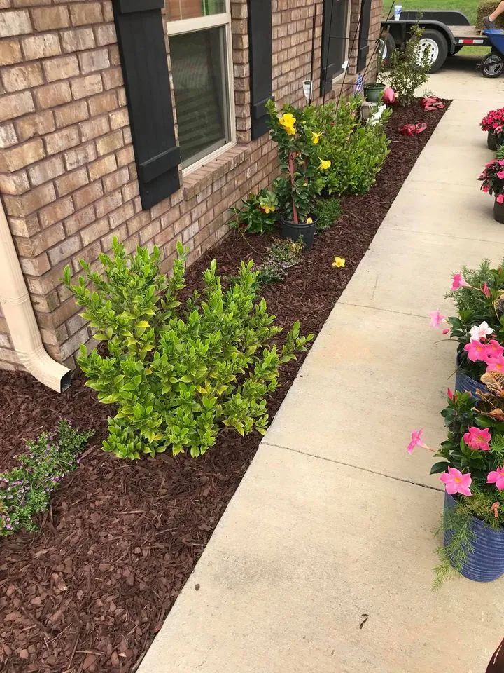 A brick house with a sidewalk and flowers in front of it.