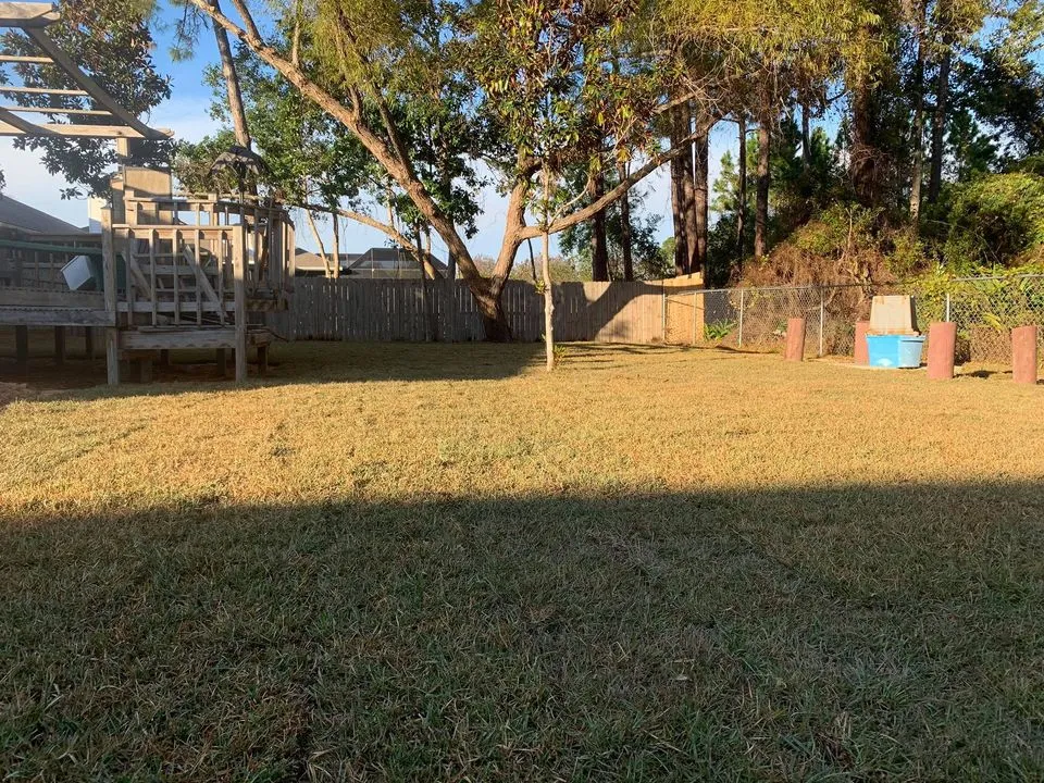 There is a playground in the backyard with a fence and trees.