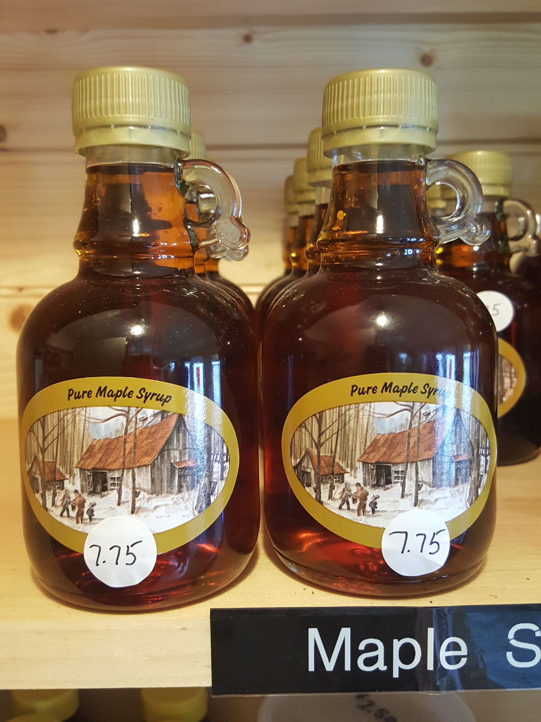 Two bottles of maple syrup are sitting on a wooden shelf.
