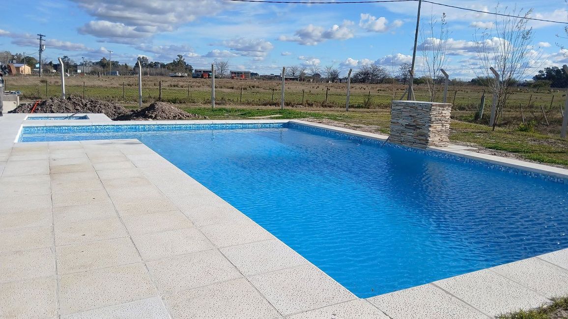 Piscina en un patio trasero iluminada en tonos azules por la noche, vista desde arriba, con luces cálidas en las paredes y baldosas en el patio.