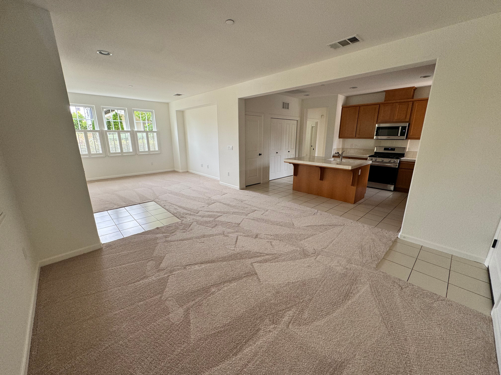 An empty living room with a kitchen in the background.