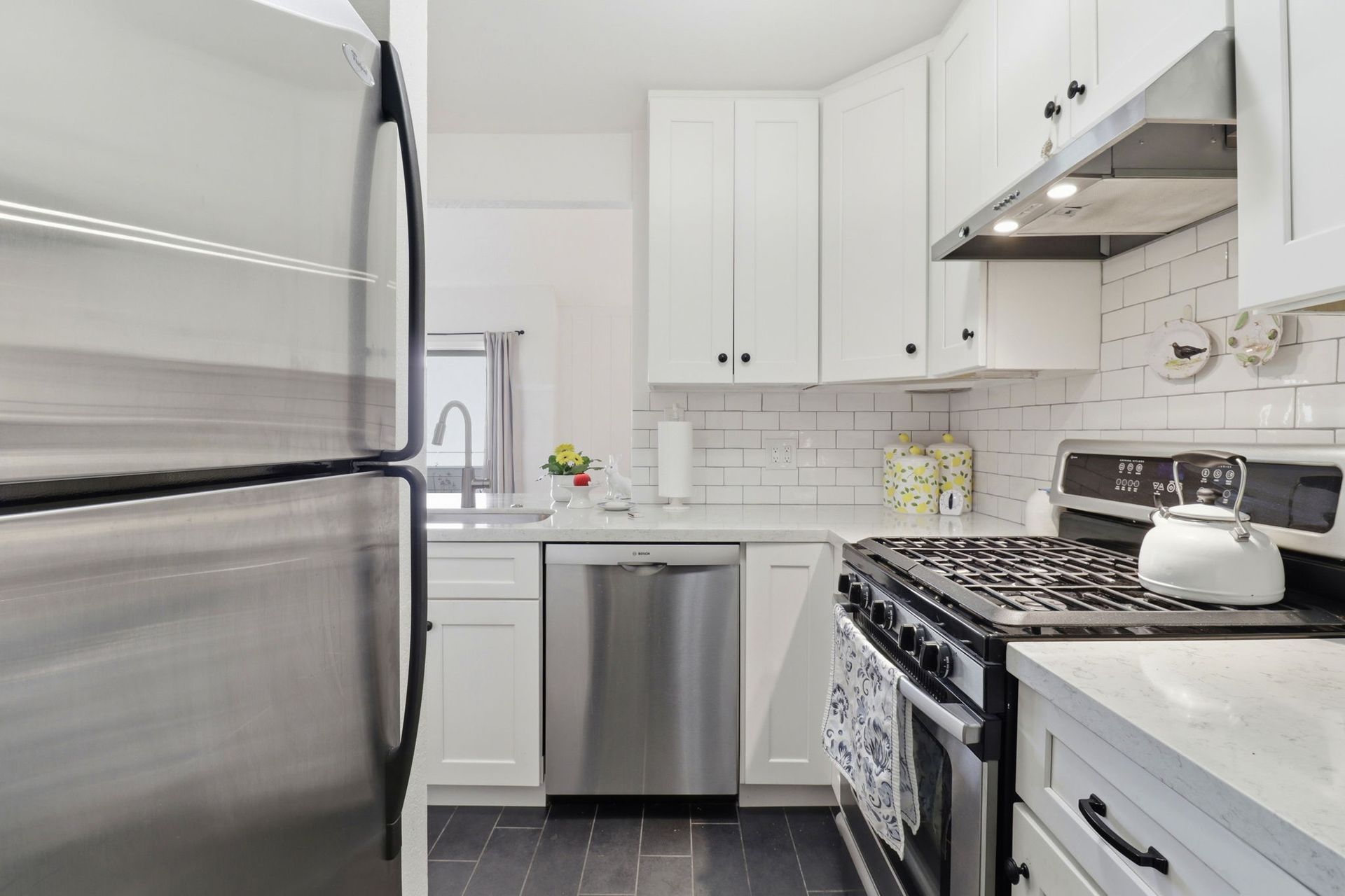 Bright white kitchen with stainless steel appliances, gas stove, and black tile floor