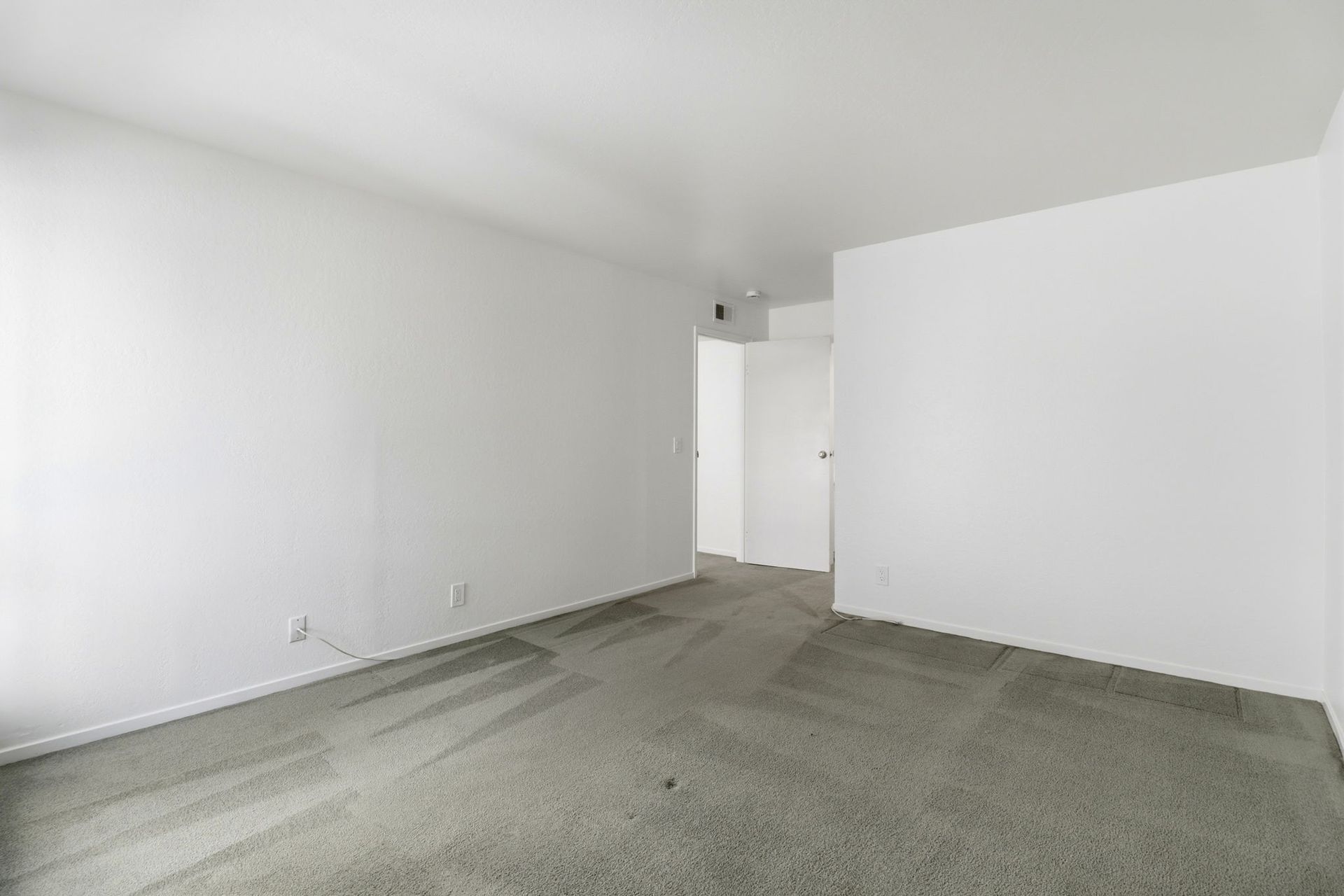 Empty white room with gray carpet and a doorway in the back wall