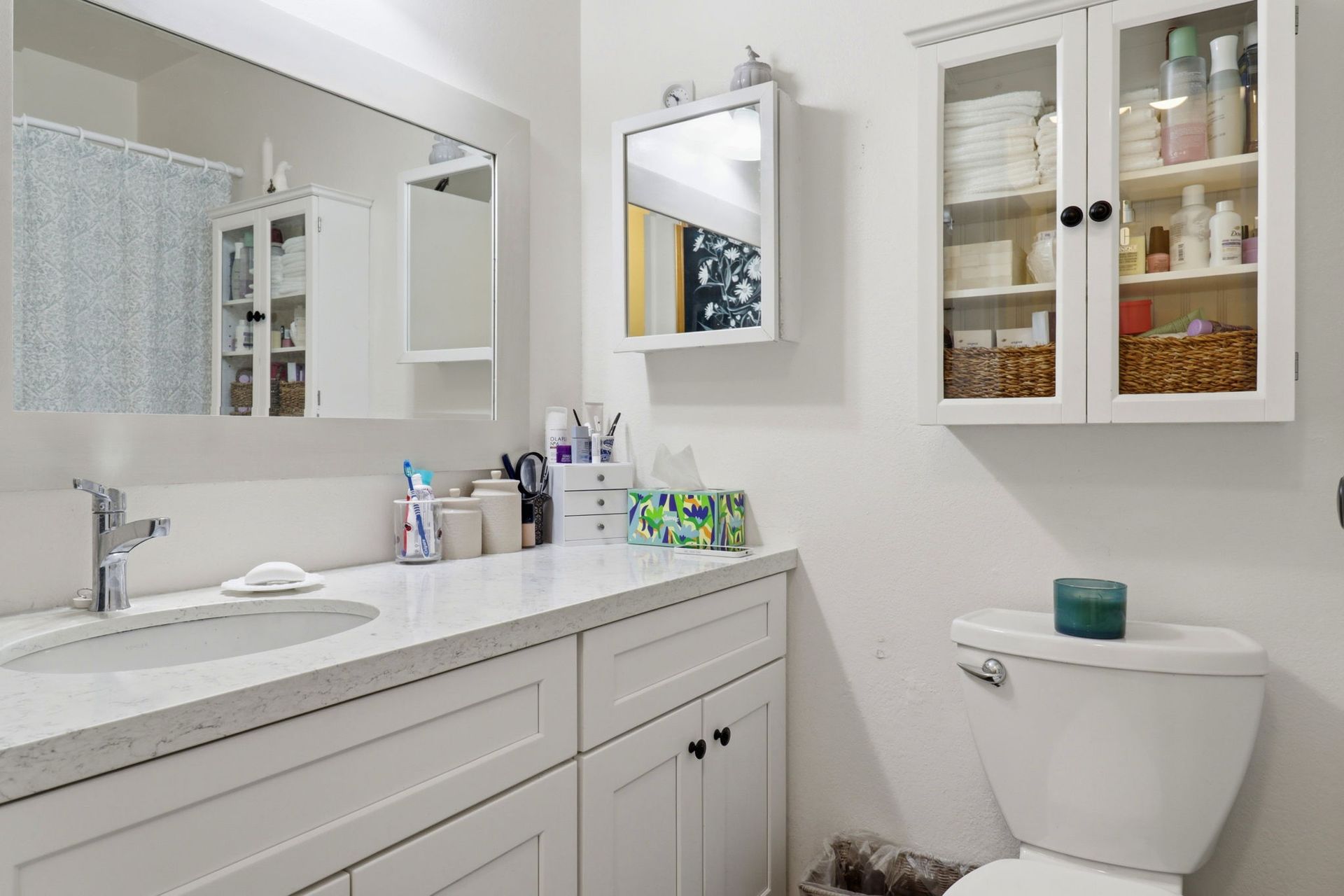 Bright white bathroom with vanity, mirror cabinets, and a toilet with a teal candle on top
