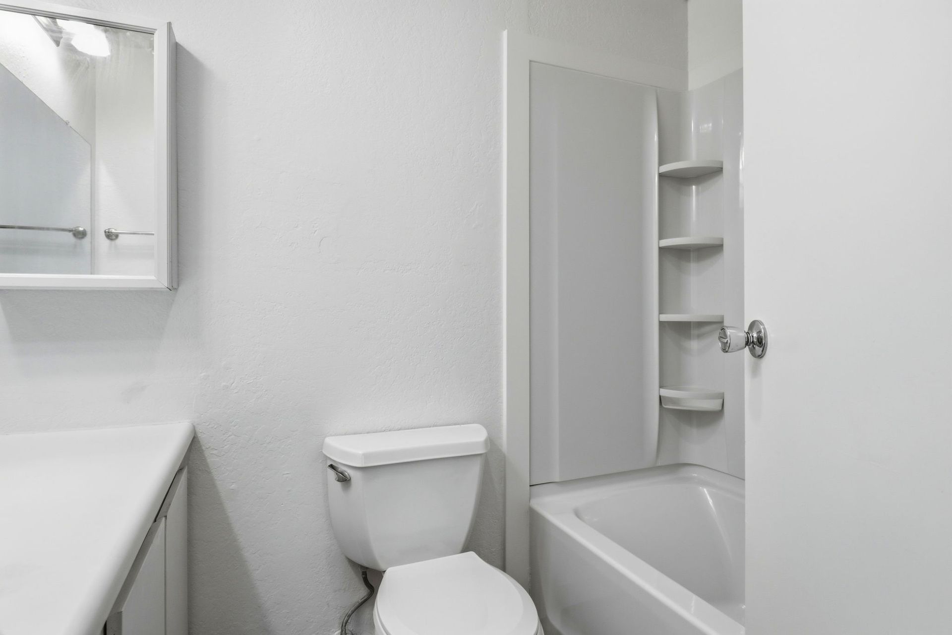 Small white bathroom with toilet, sink, mirror, and bathtub shower combo