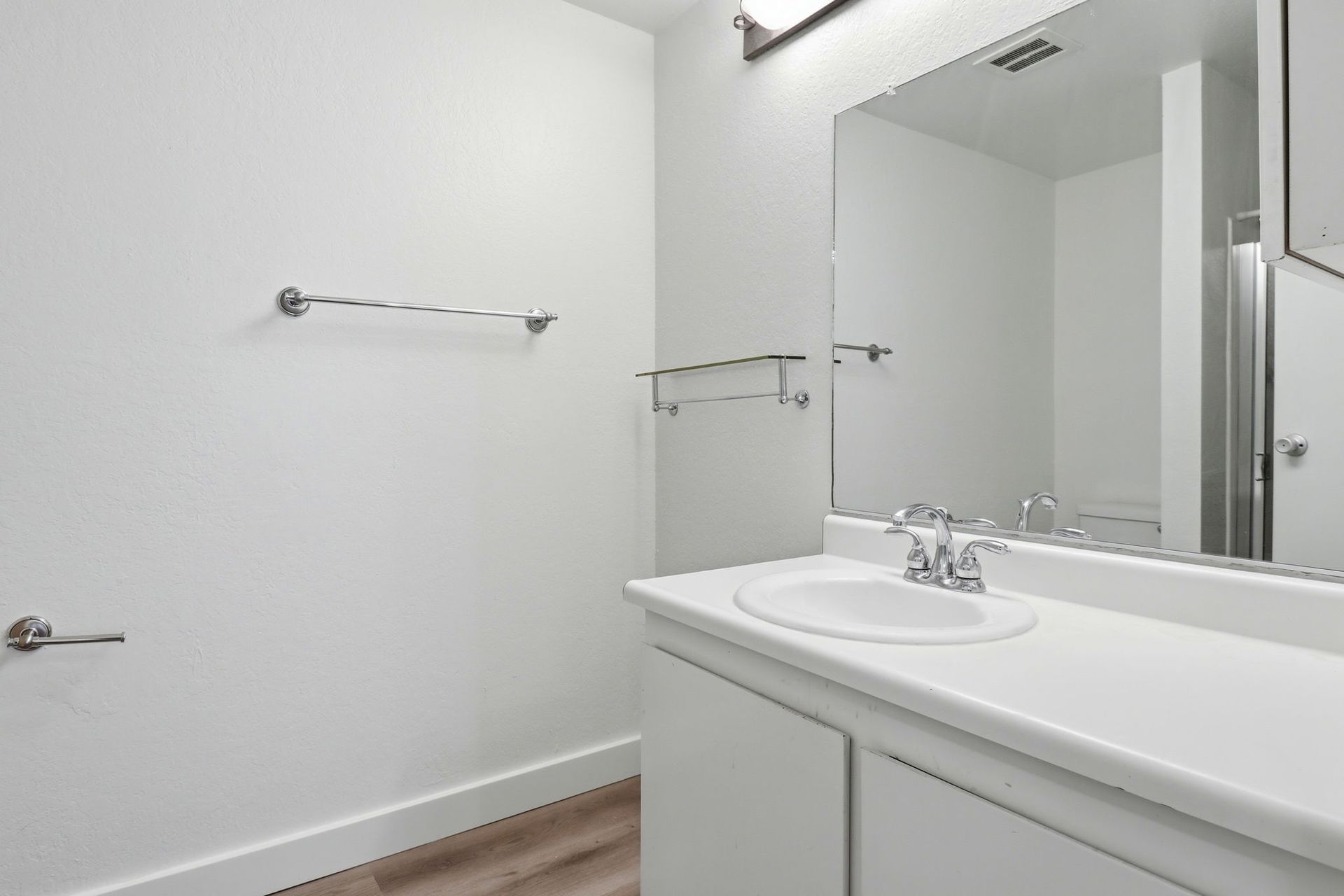 Bright bathroom vanity with sink and large mirror, white walls, towel bars, and wood floor
