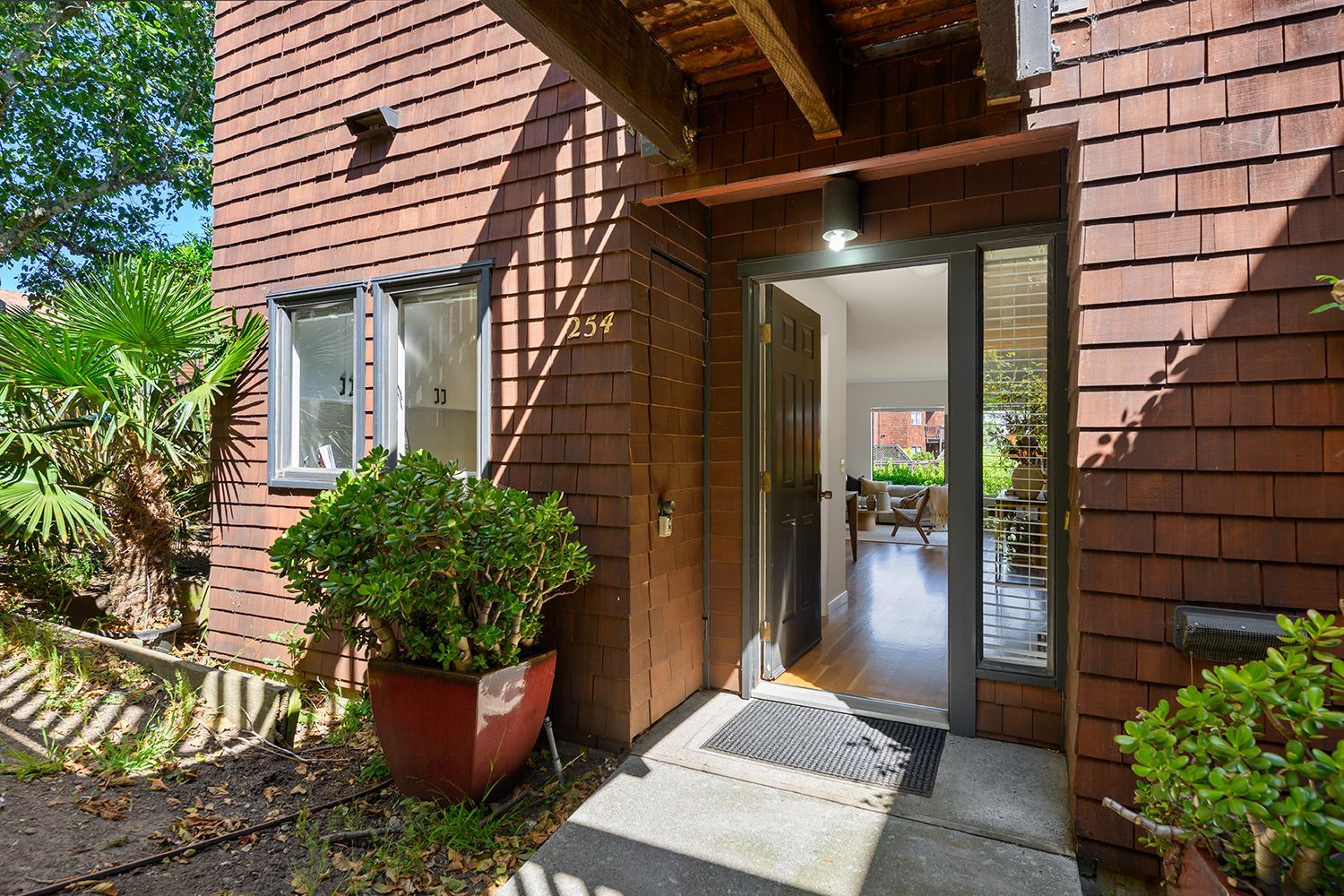 Front entrance to a brick house with open door, potted plants, and a small stone walkway.