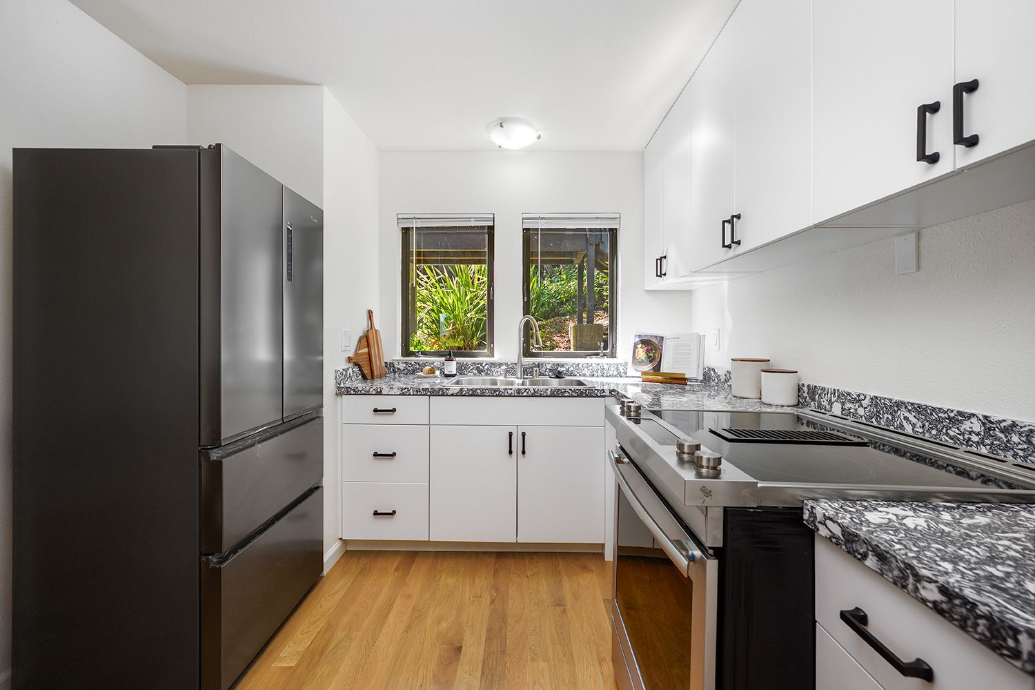Compact modern kitchen with dark appliances, white cabinets, granite counters, and a window over the sink.