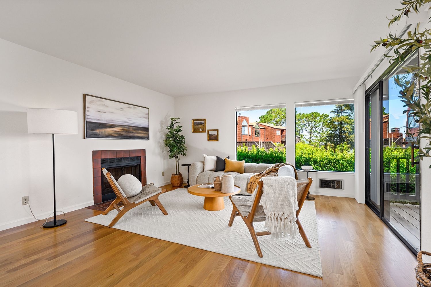 Bright living room with wicker chairs, rug, fireplace, and large windows opening to a garden.
