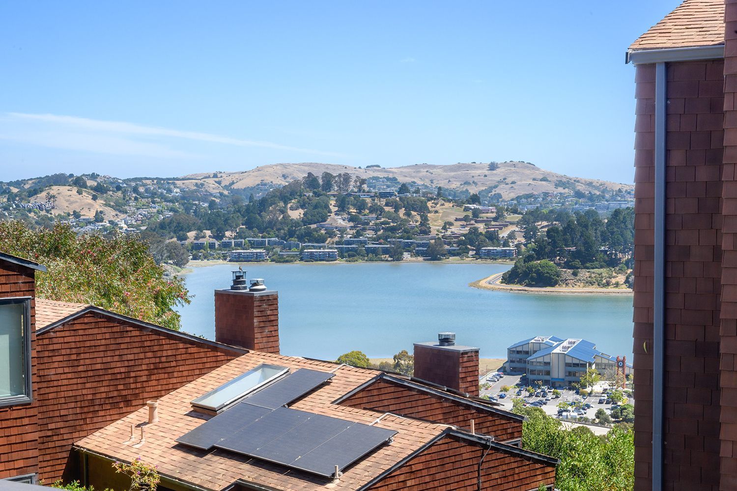 View of a bay and hillside town, framed by red-tiled rooftops and a clear blue sky