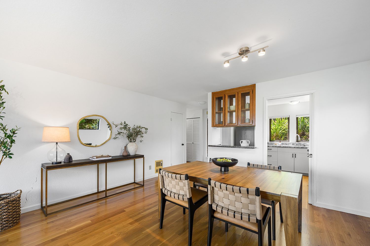 Bright dining room with wooden table, chairs, sideboard, and kitchen visible in the background.