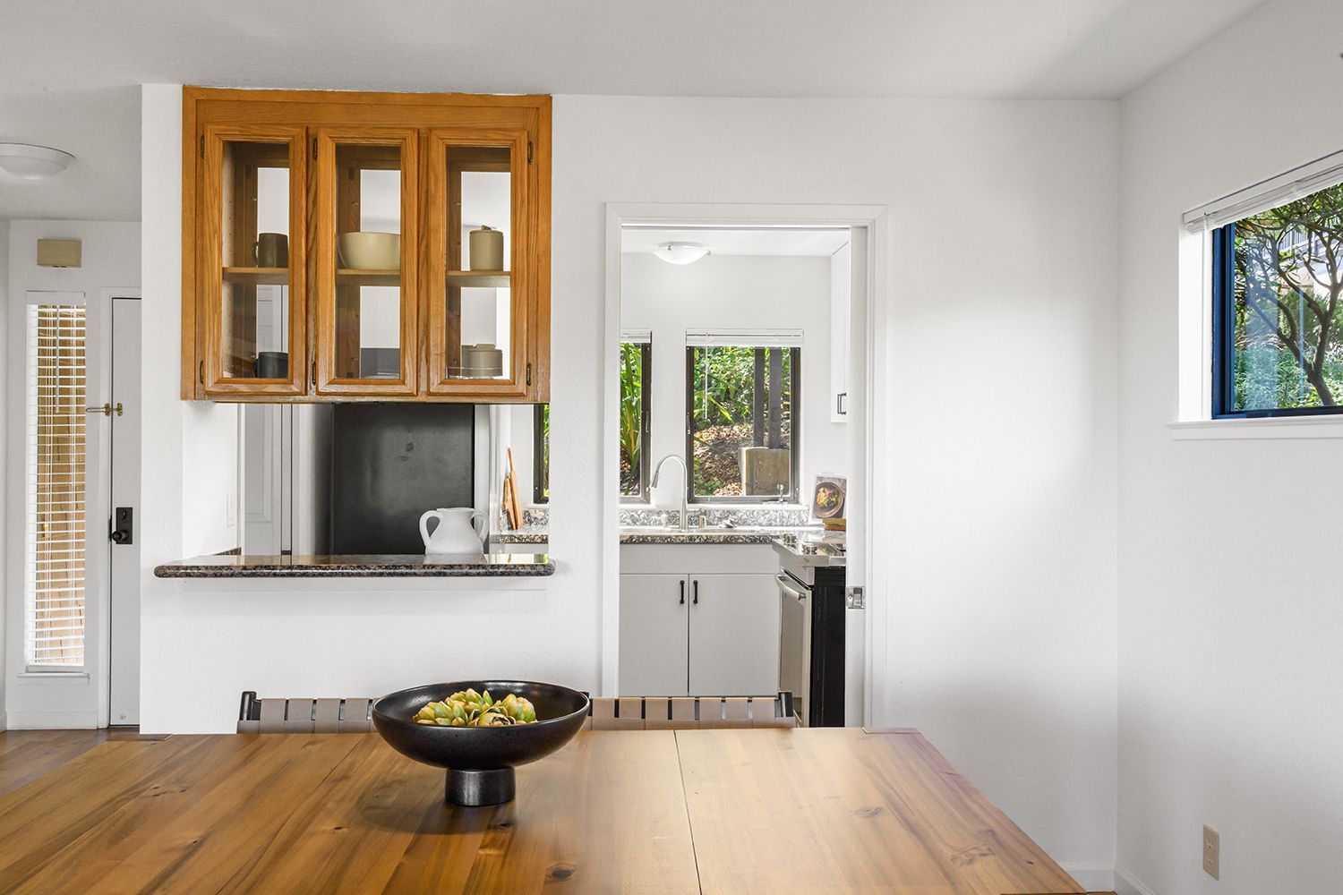 Bright kitchen with wooden cabinets, white walls, and a dining table with a fruit bowl.