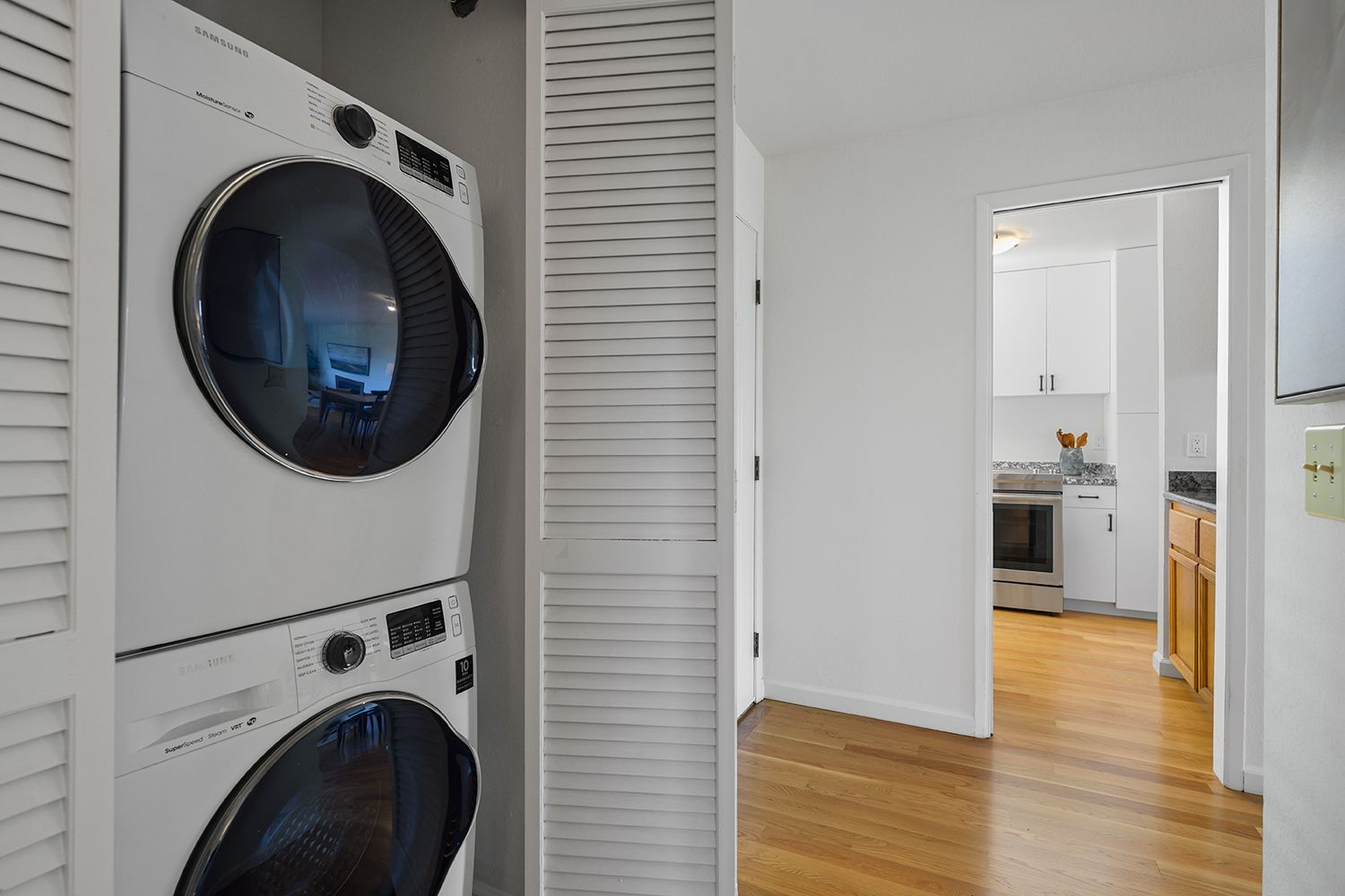 Stacked washer and dryer in a closet beside a bright hallway leading to a kitchen