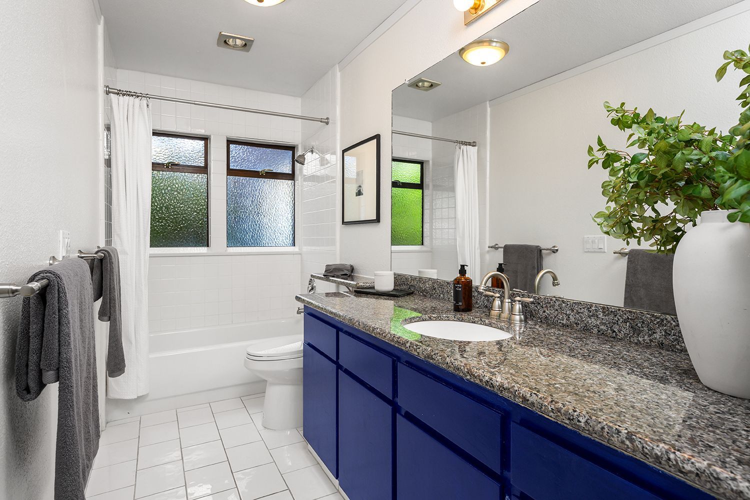 Bright bathroom with navy vanity, speckled countertop, white tile, and window above the tub.