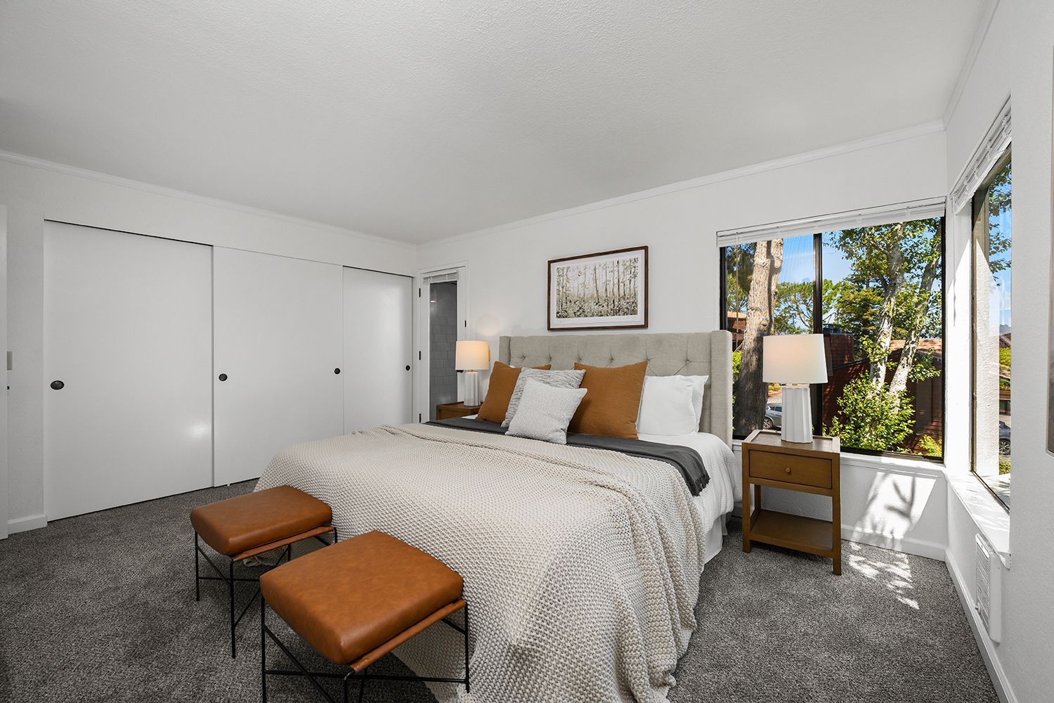 Bright bedroom with a large bed, gray carpet, white closet doors, and sunlight from a window
