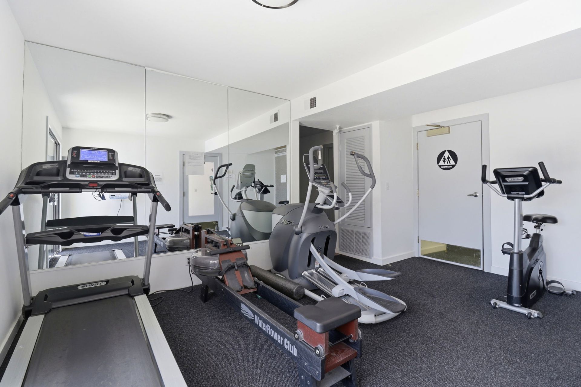 Bright home gym with treadmill, elliptical, stationary bike, and mirrored wall