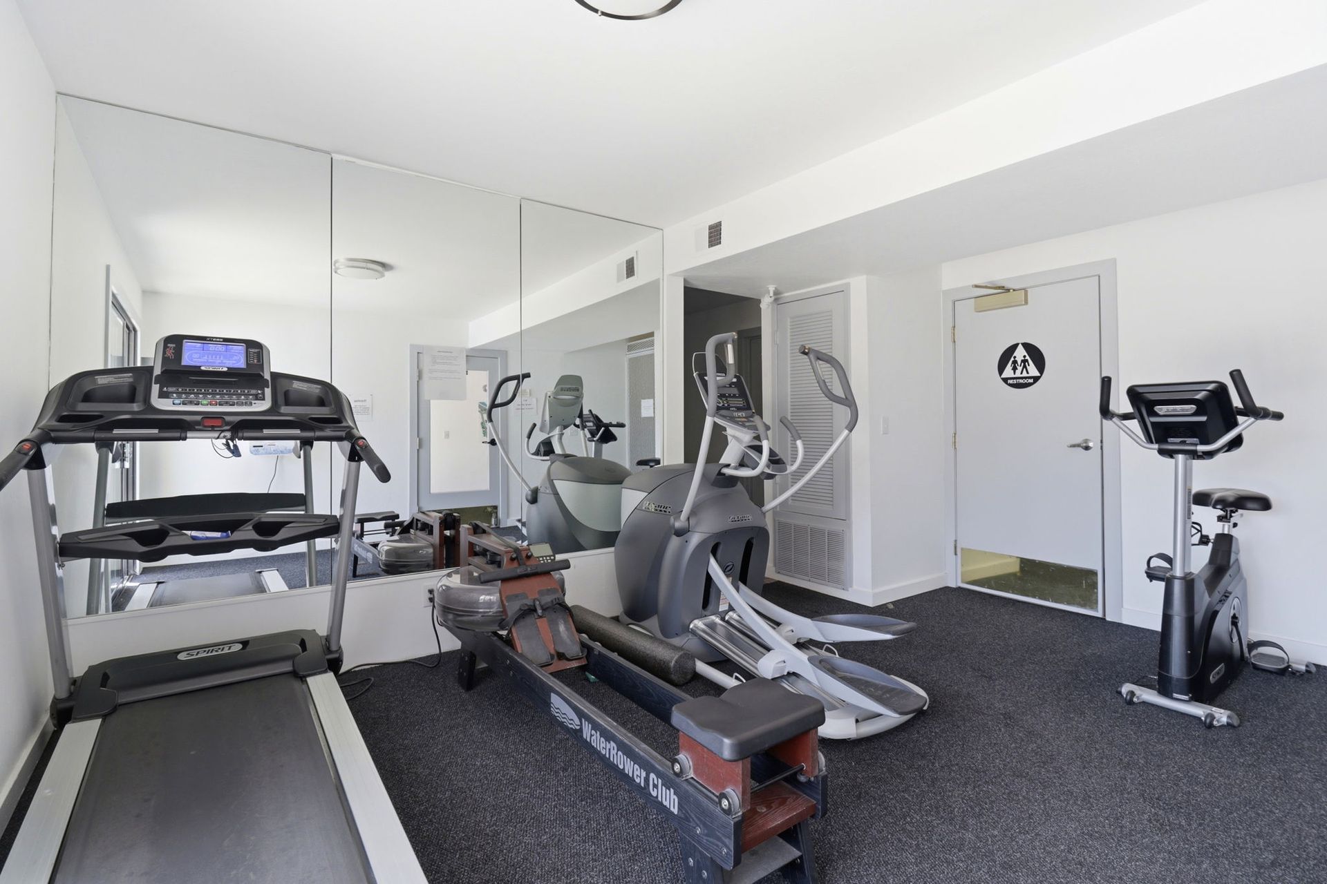 Home gym with treadmill, elliptical, stationary bike, and mirrored walls
