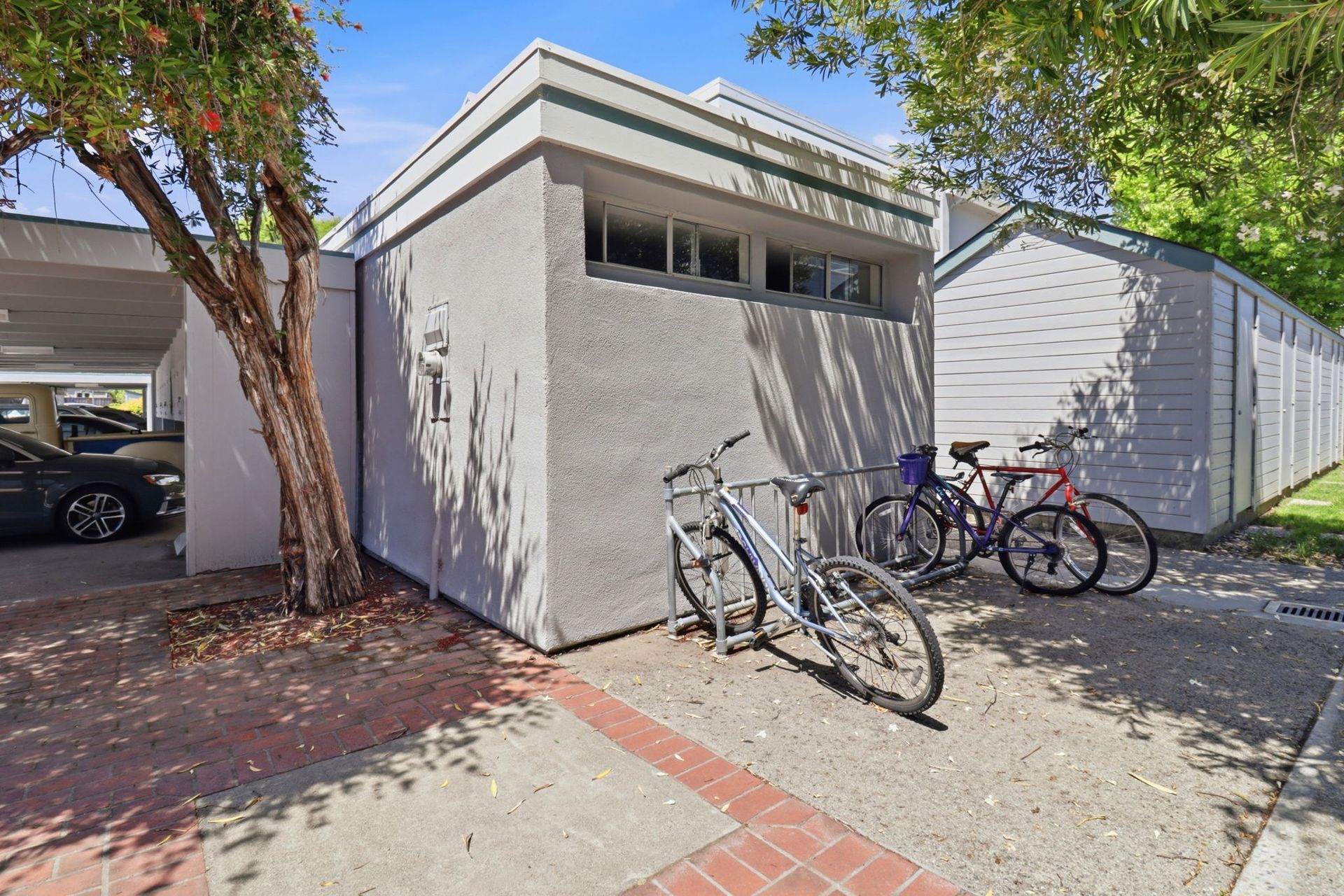 Bike rack beside a gray building with several parked bicycles in a sunny courtyard