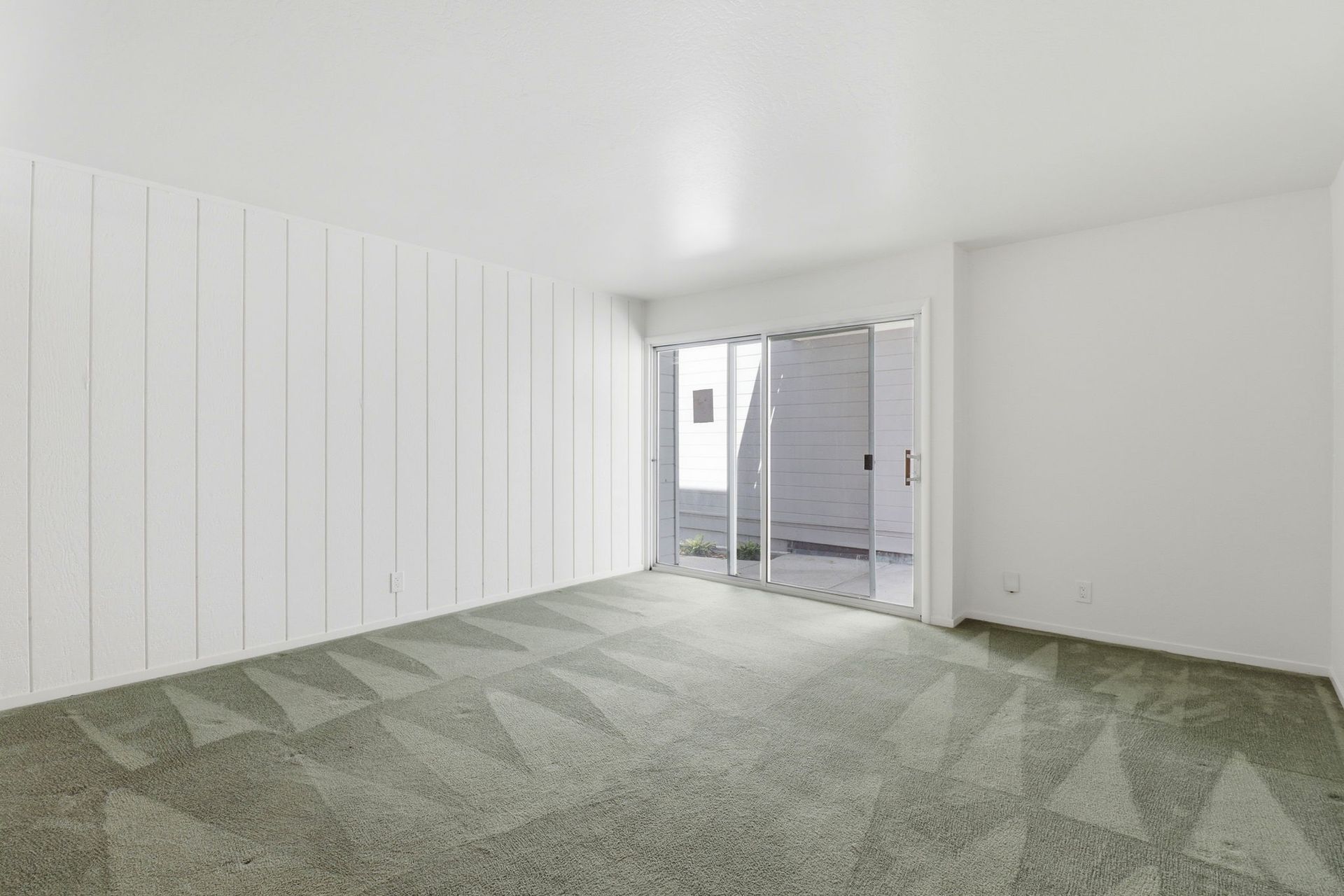 Empty white room with green carpet and sliding glass doors to a patio