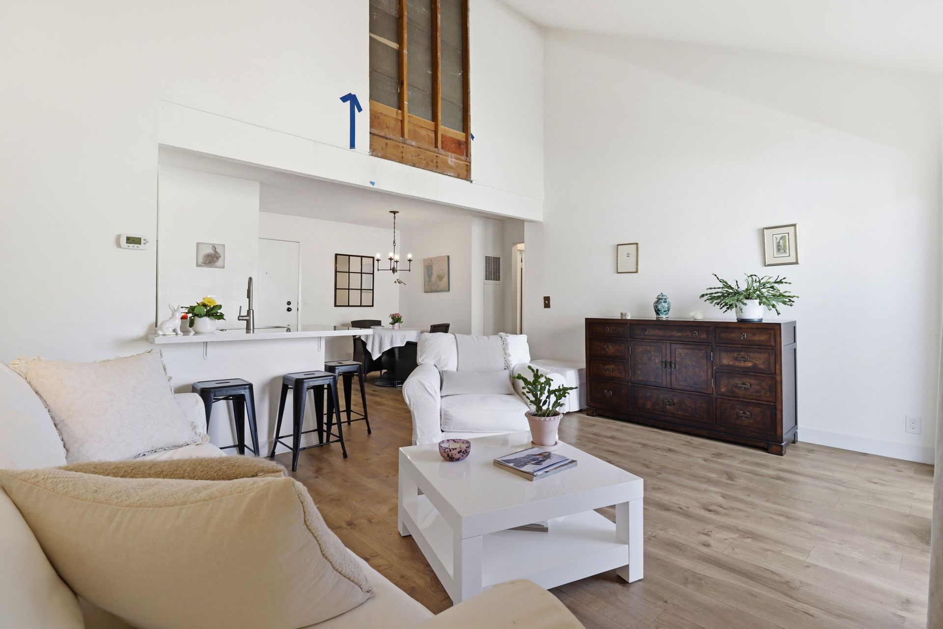 Bright living room with white furniture, dining area, and dark sideboard on light wood floor